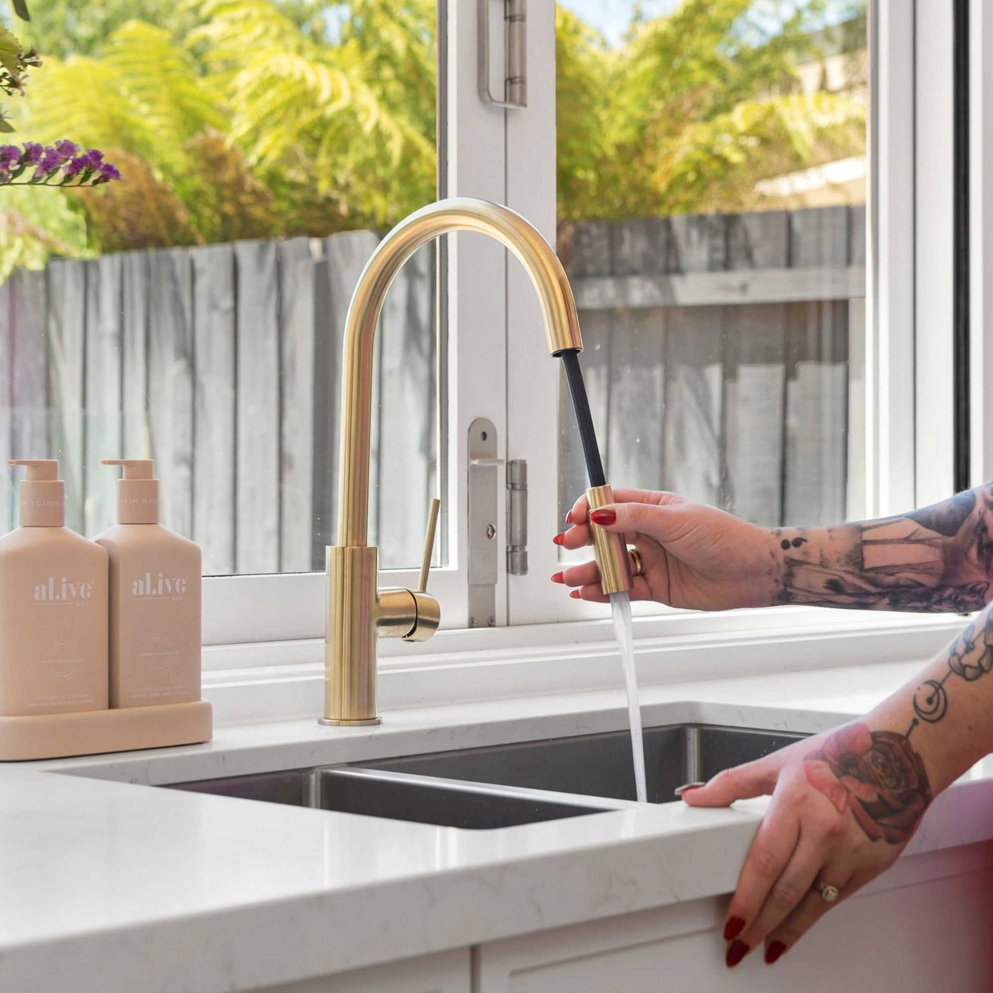 Person using a brushed gold kitchen laundry pull out mixer tap with a window and countertop in the background