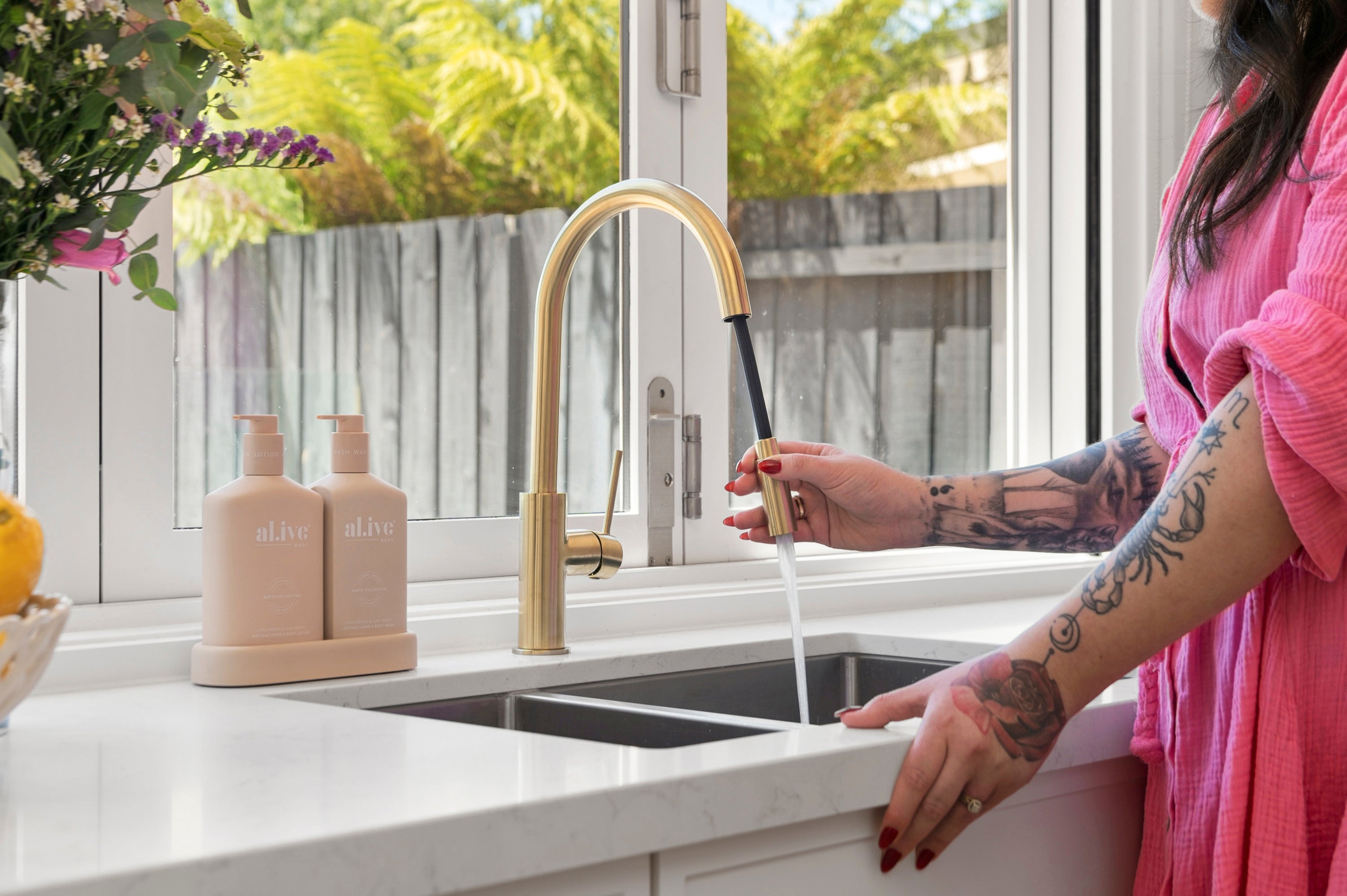 Person using a brushed gold kitchen laundry pull out mixer tap with a window and countertop in the background