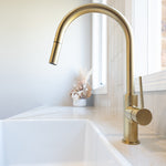 a brushed gold kitchen laundry pull out mixer tap  on a white stone laundry bench