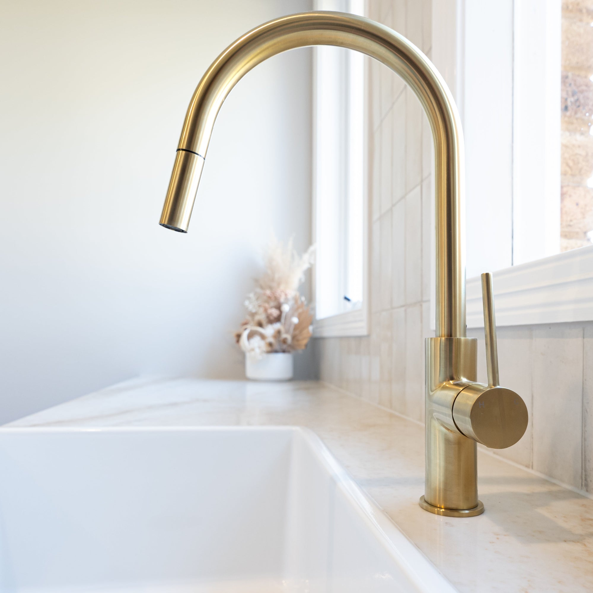 a brushed gold kitchen laundry pull out mixer tap  on a white stone laundry bench