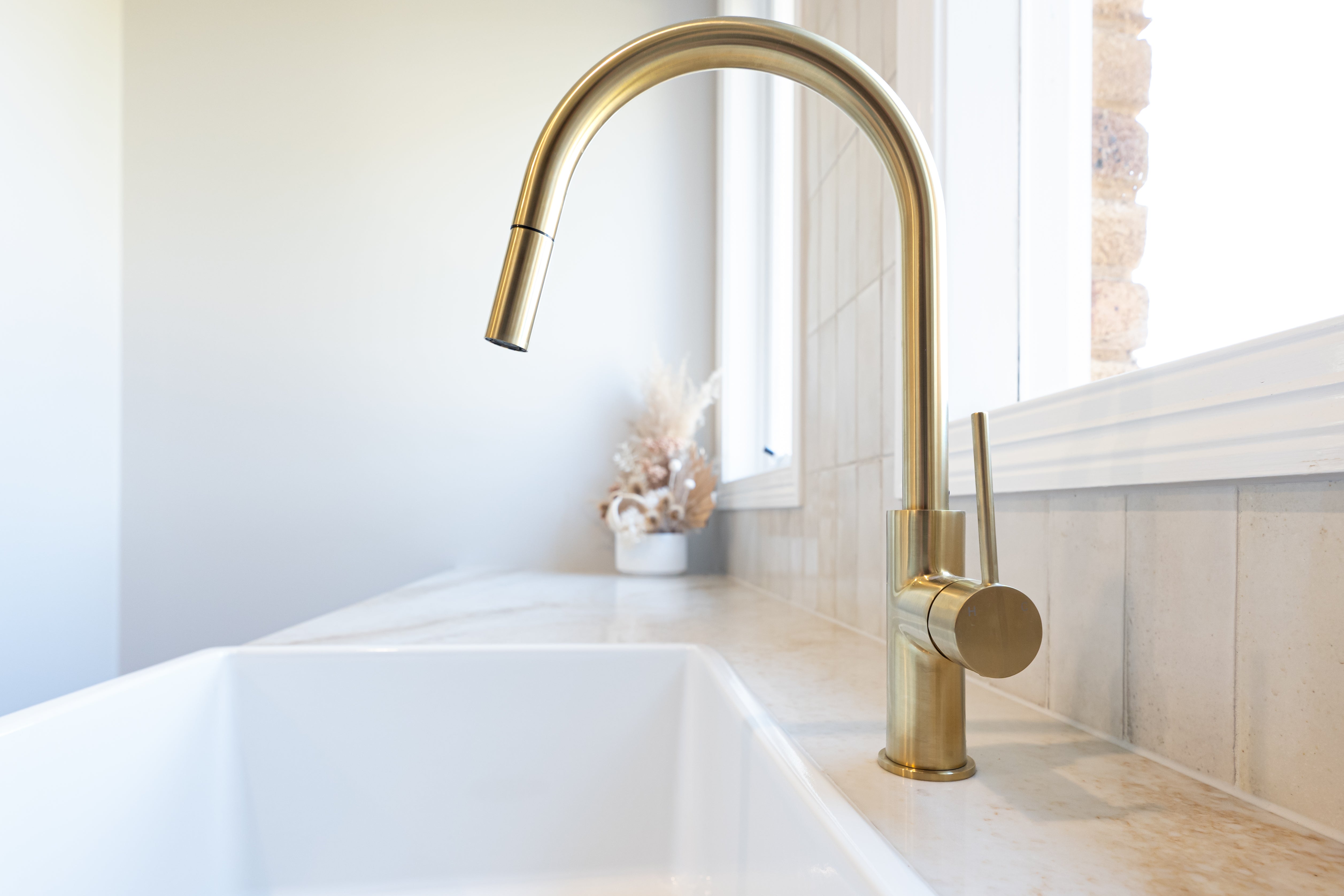 a brushed gold kitchen laundry pull out mixer tap  on a white stone laundry bench