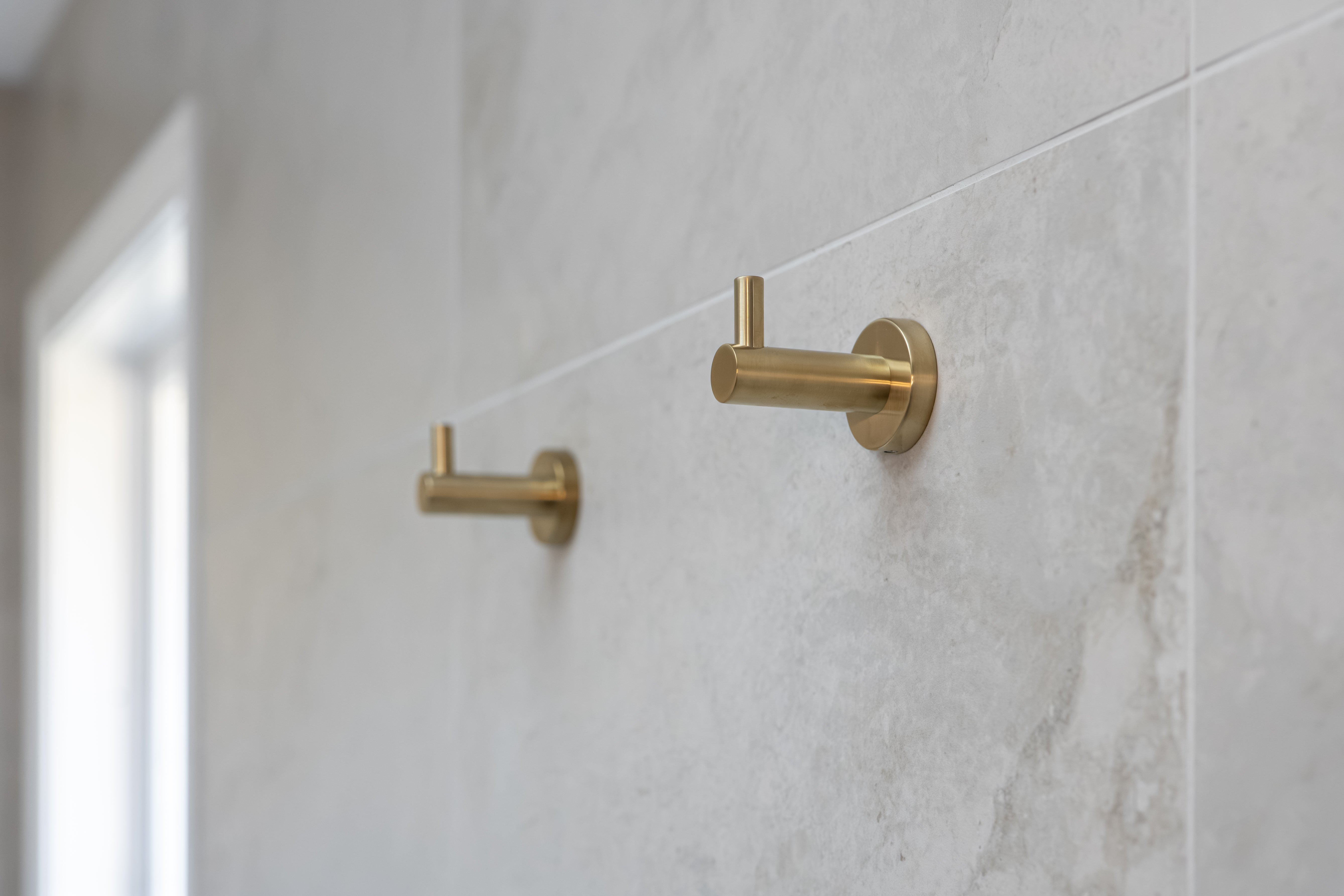 Brush gold robe hooks on a tiled wall