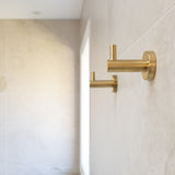 two brushed gold robe hooks mounted on a tiled wall