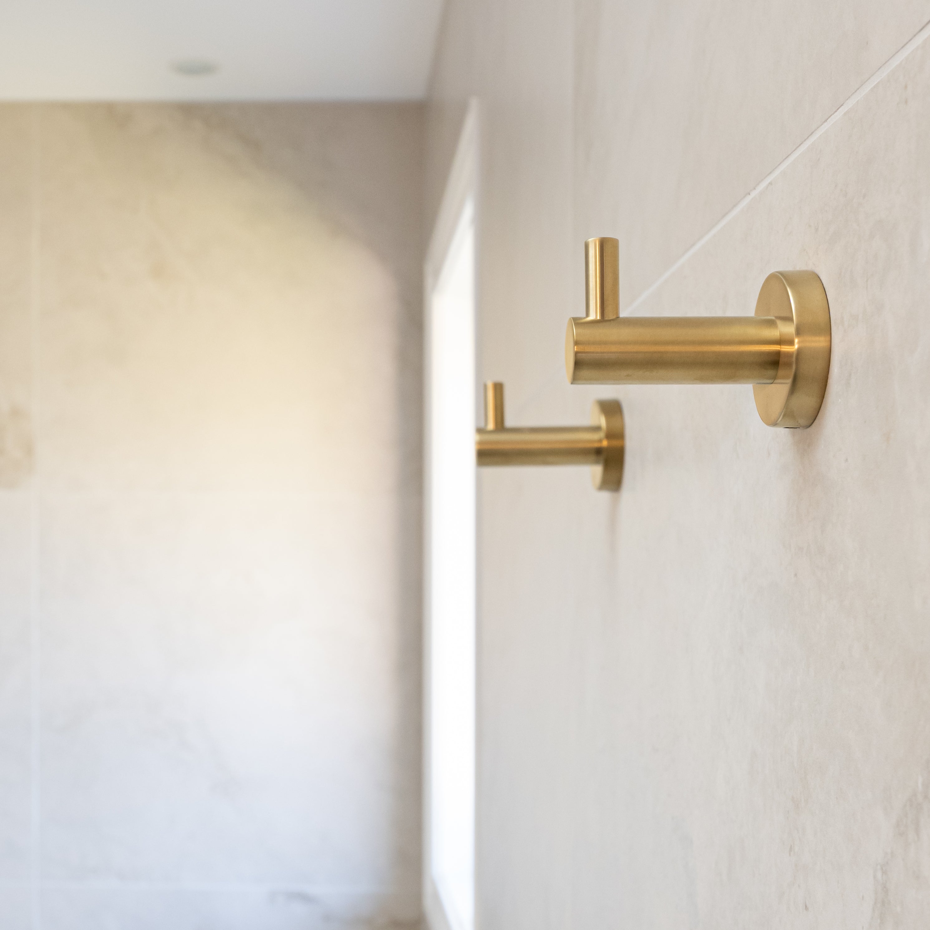 two brushed gold robe hooks mounted on a tiled wall