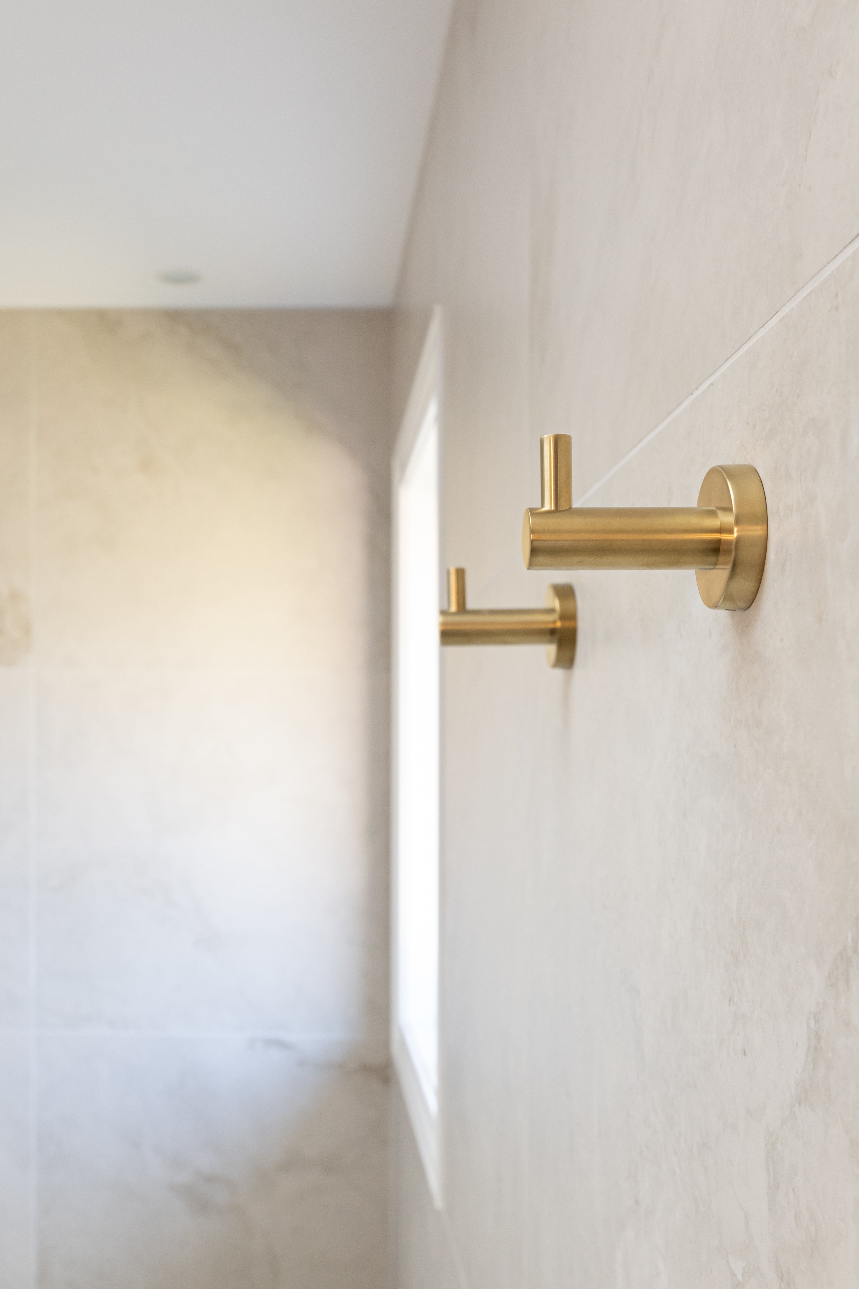 two brushed gold robe hooks mounted on a tiled wall