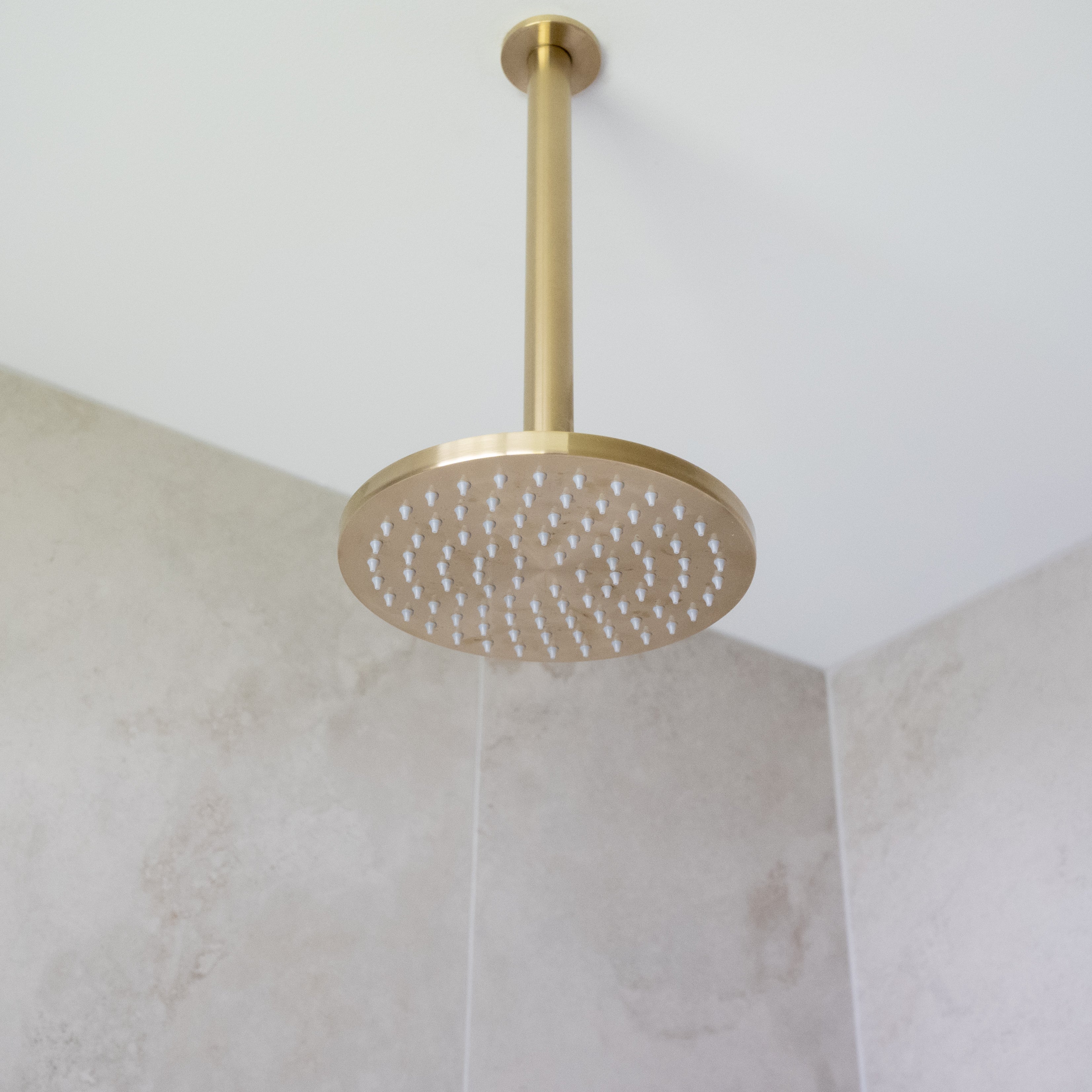 a brushed gold shower arm mounted from the ceiling with a brushed gold shower head