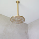 a brushed gold shower head on a gold arm mounted from a white ceiling