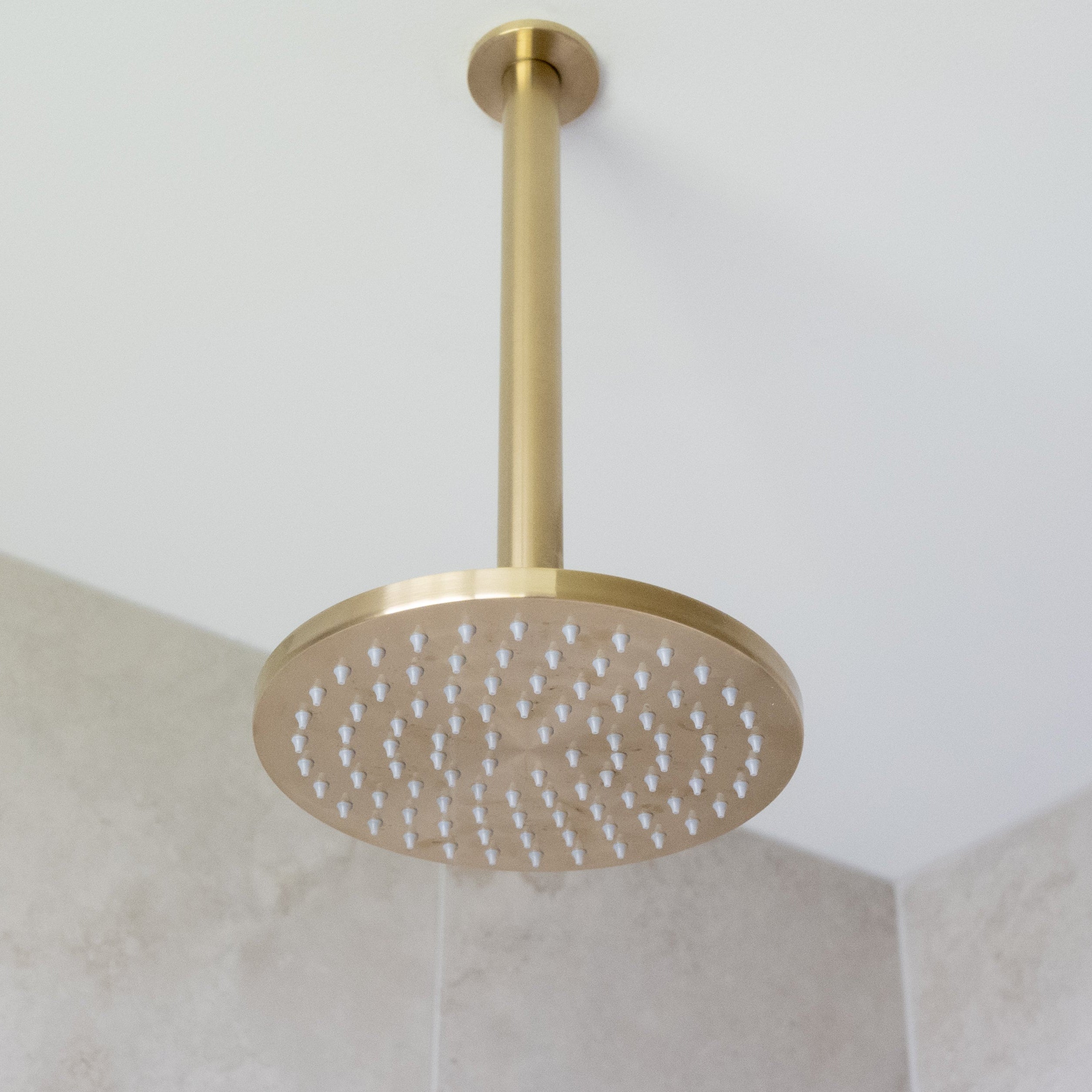 a brushed gold shower head on a gold arm mounted from a white ceiling