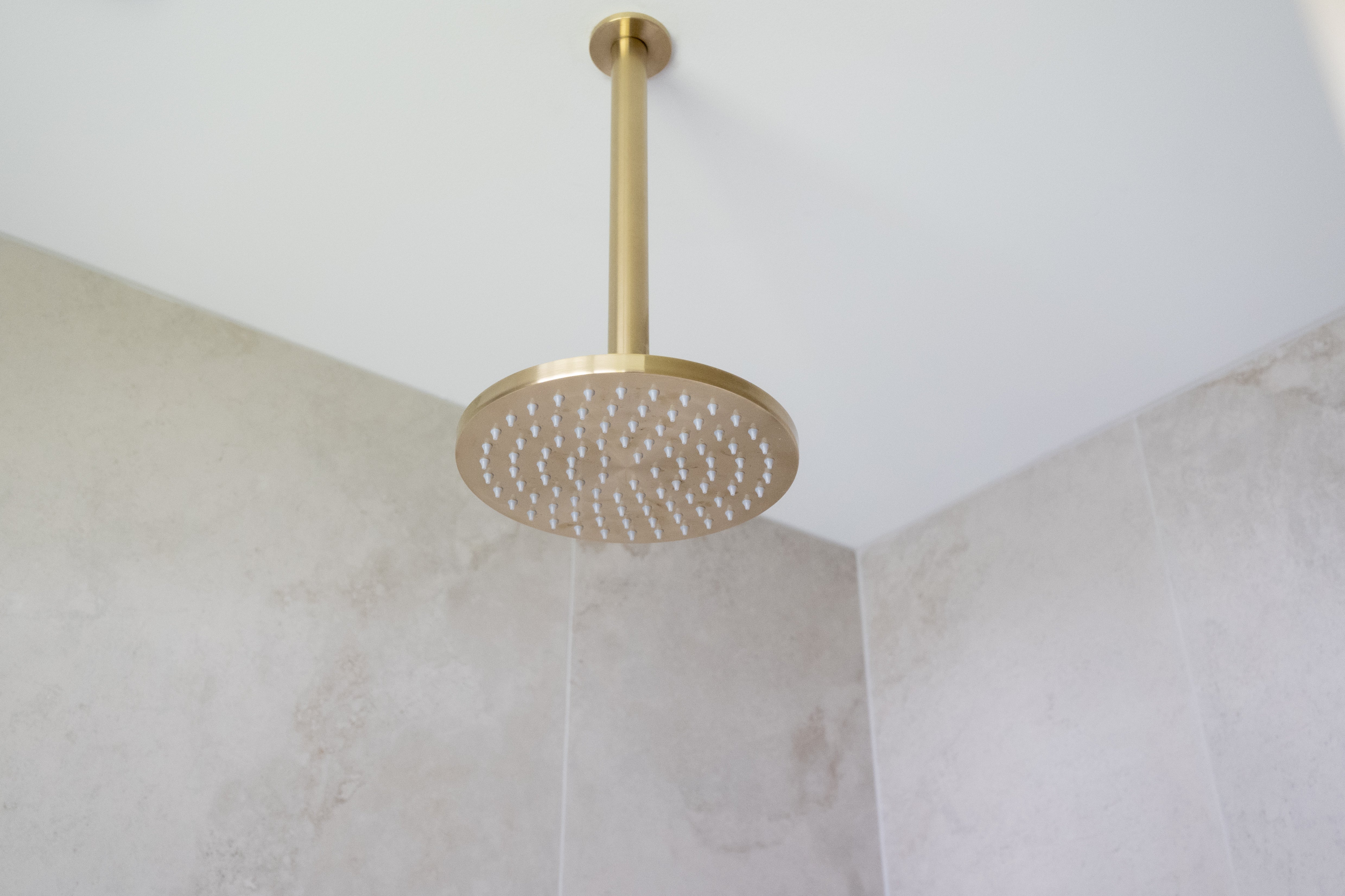a brushed gold shower head on a gold arm mounted from a white ceiling