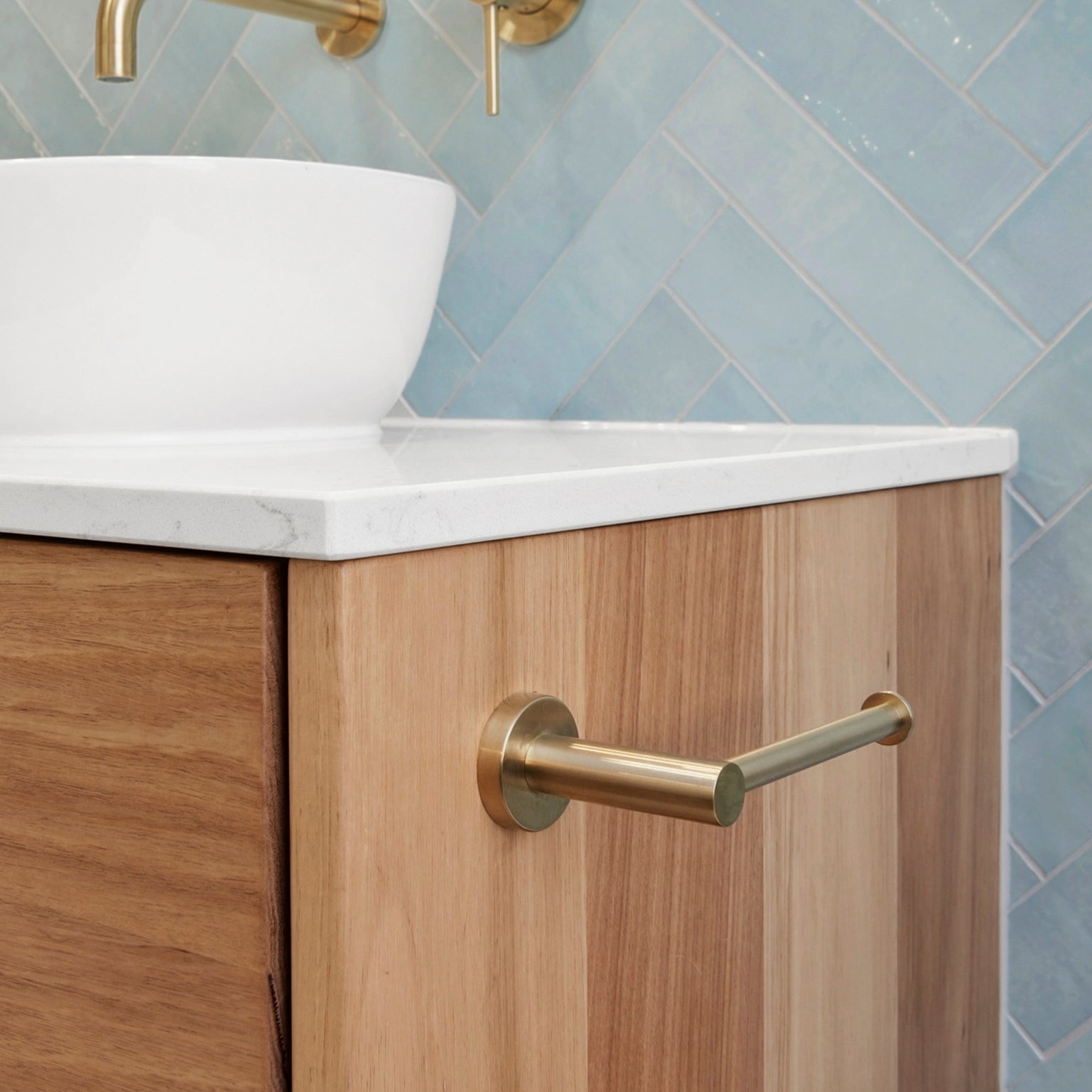 brushed gold toilet roll holder mounted on a white stone and timber vanity with blue tiles in the background