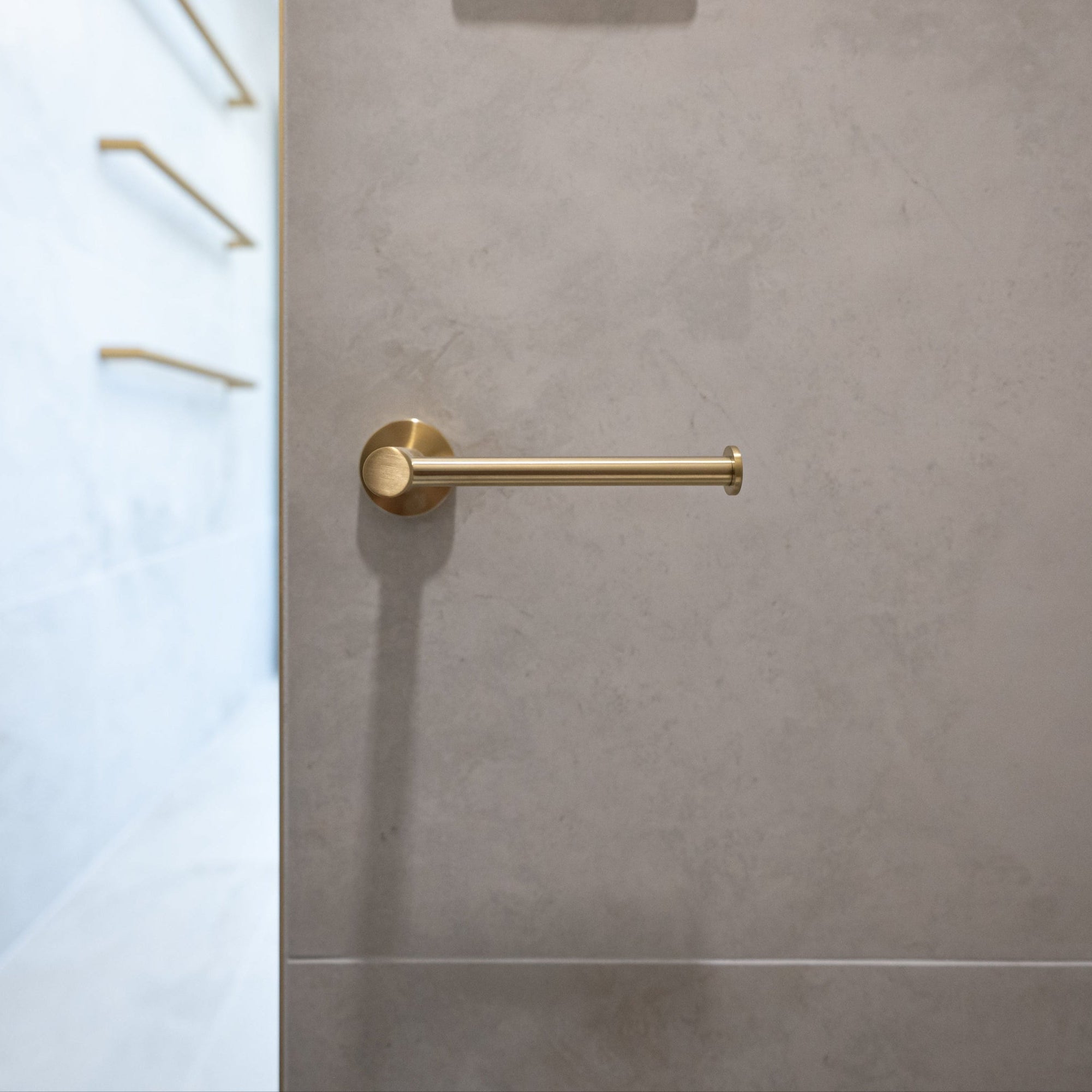 Brushed gold toilet roll holder mounted on a tiled bathroom wall.
