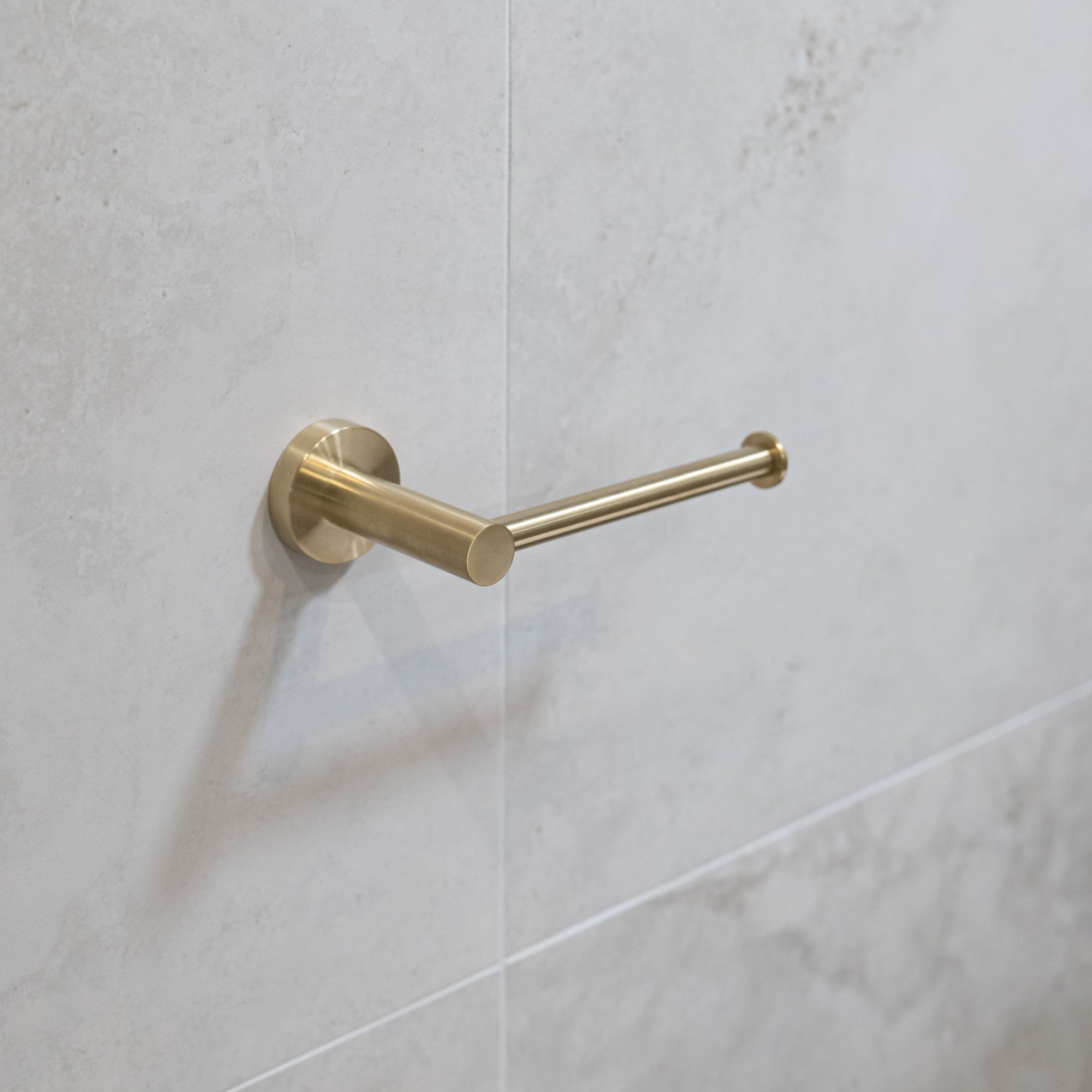 Brushed gold toilet roll holder on a tiled wall