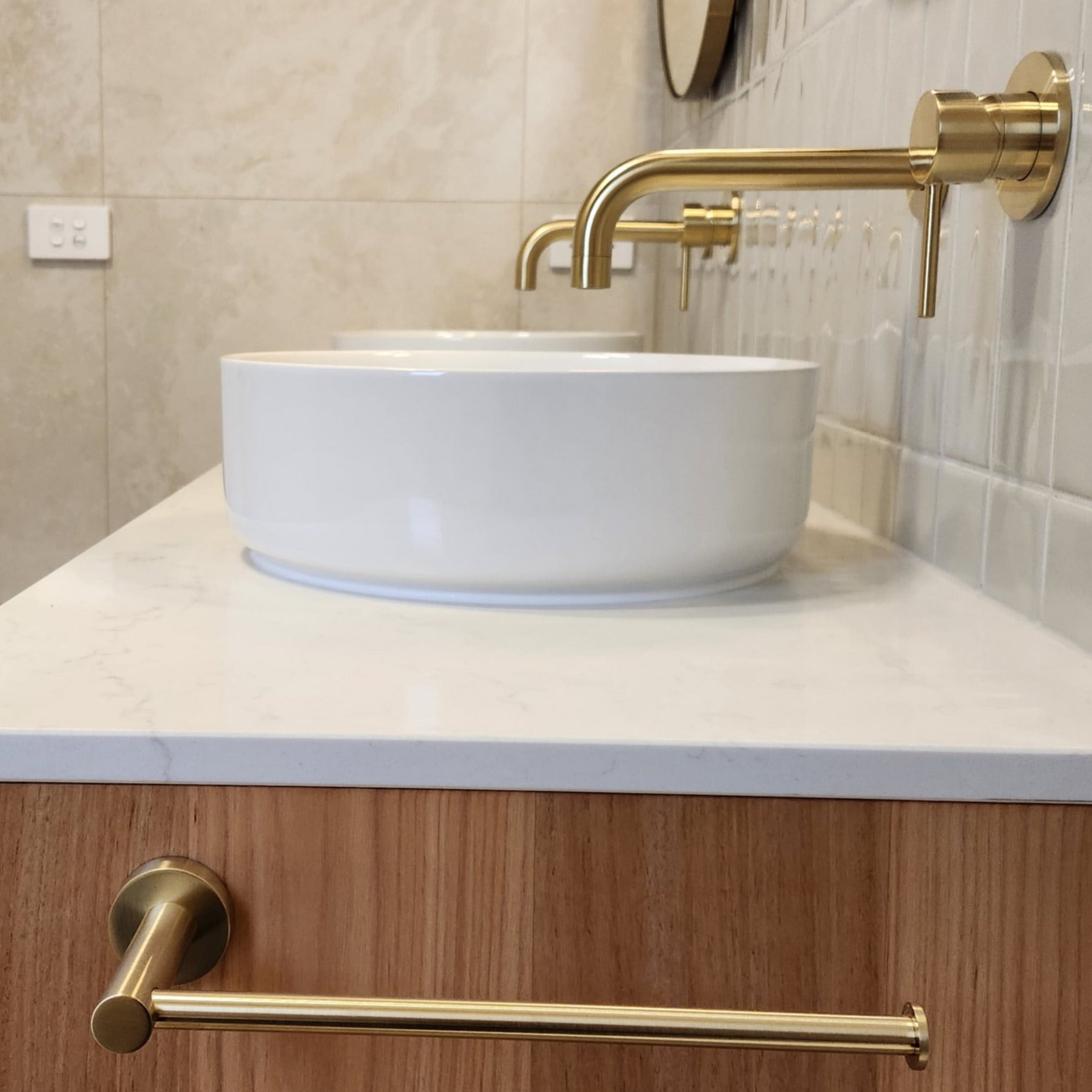 a brushed gold towel holder on bathroom vanity with white sink, brushed gold faucet,  and wooden cabinet