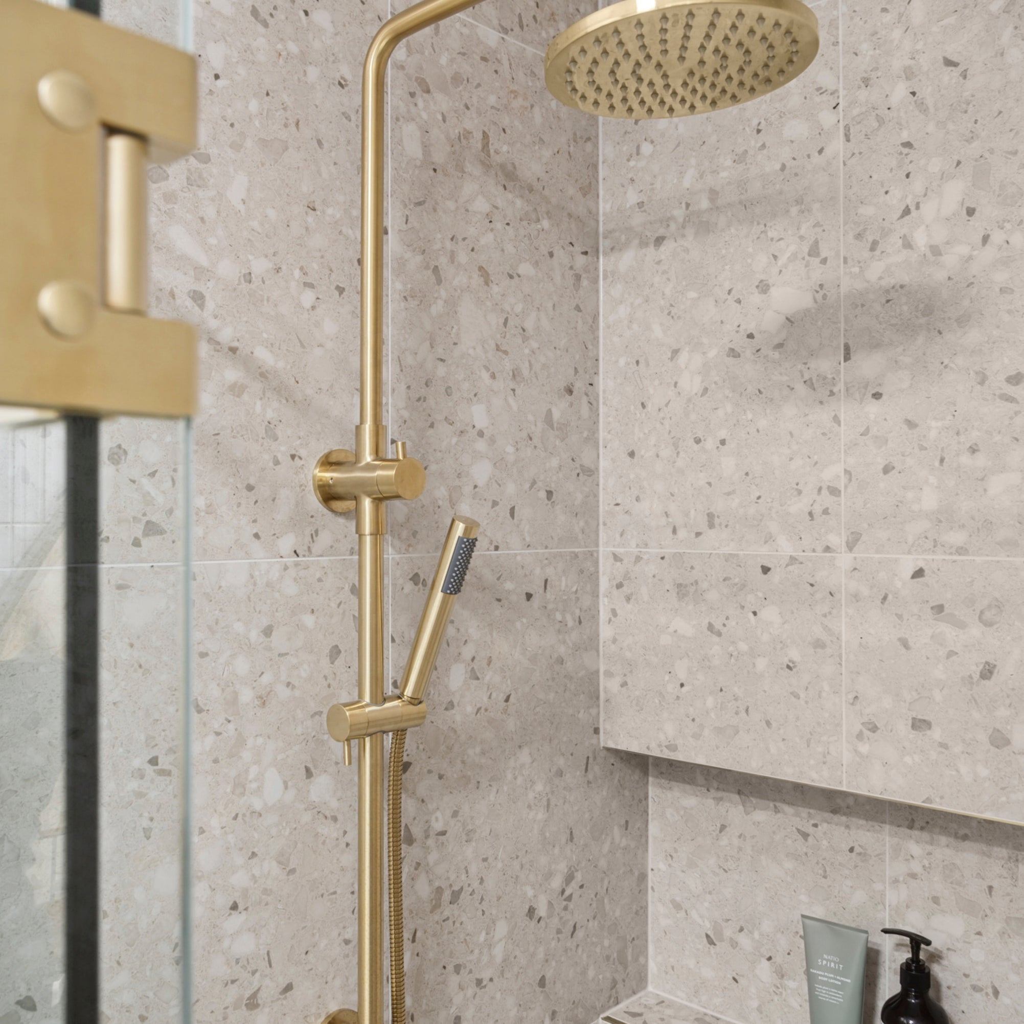 brushed gold twin round combination shower rail with diverter on a terazzo tile background