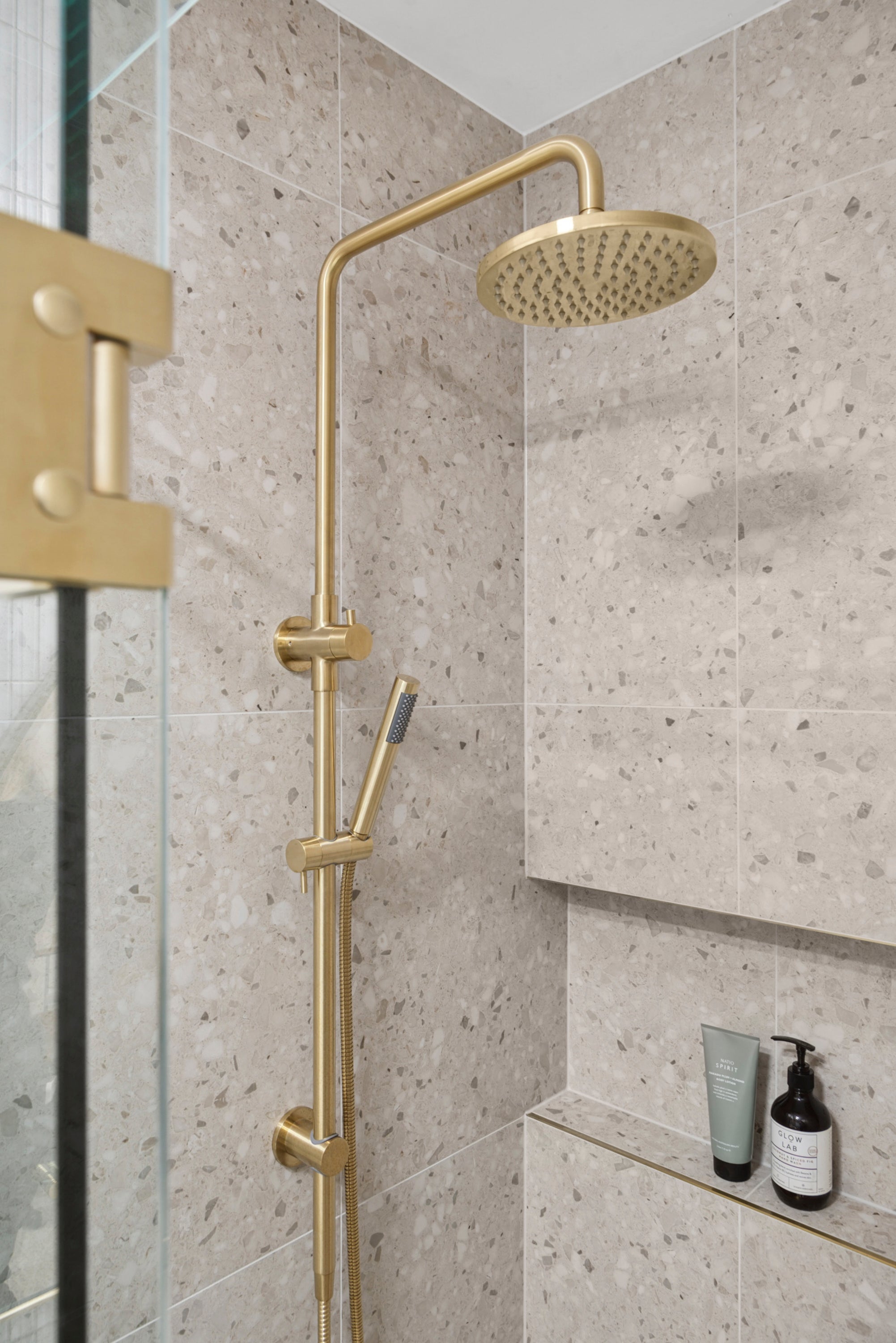 brushed gold twin round combination shower rail with diverter on a terazzo tile background