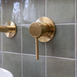 a brushed gold wall mixer on a green tiled backround
