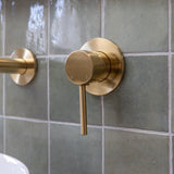 a brushed gold wall mixer on a green tiled backround