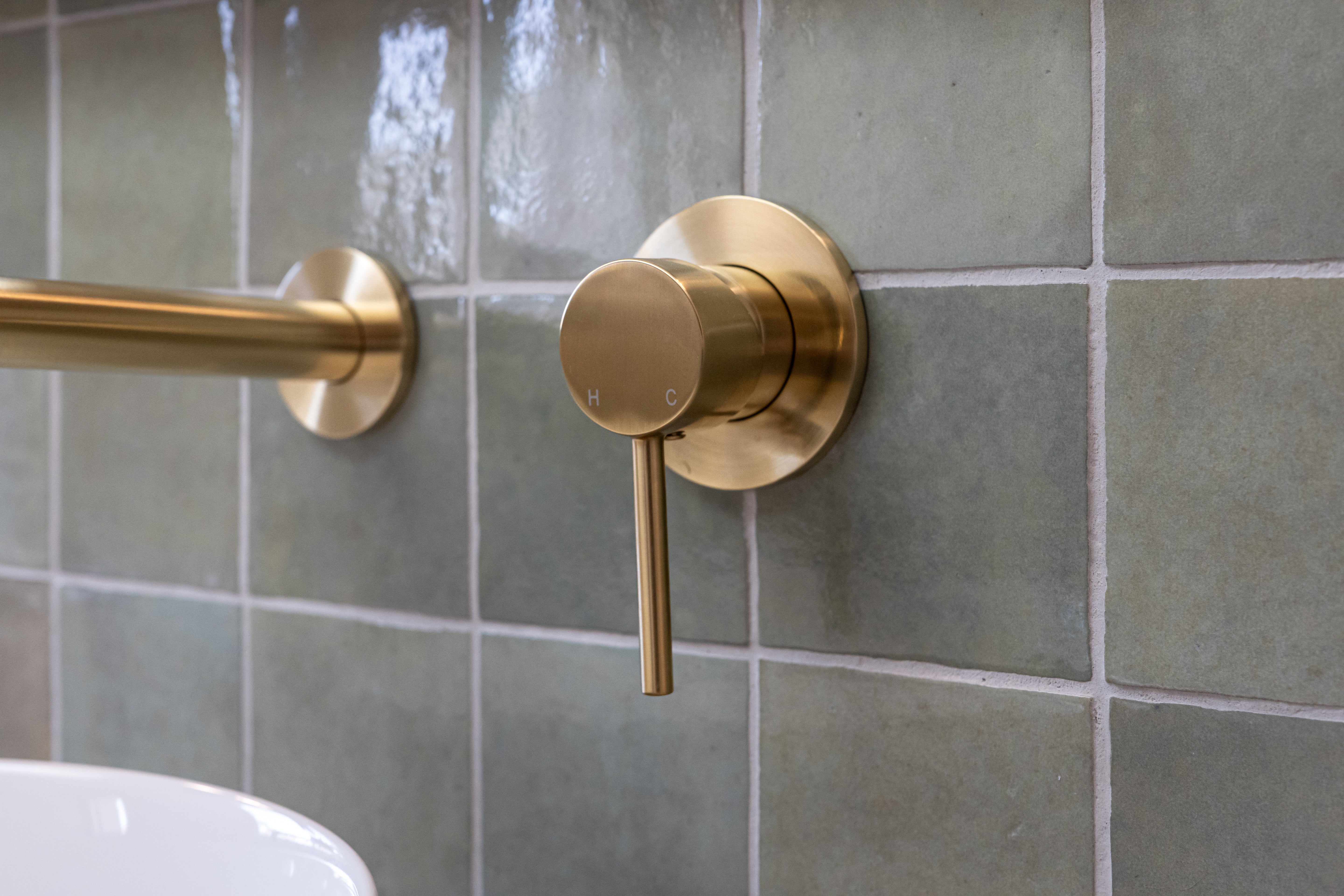a brushed gold wall mixer on a green tiled backround