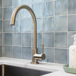 a brushed nickel kitchen laundry mixer on a white bench with a blue tile background