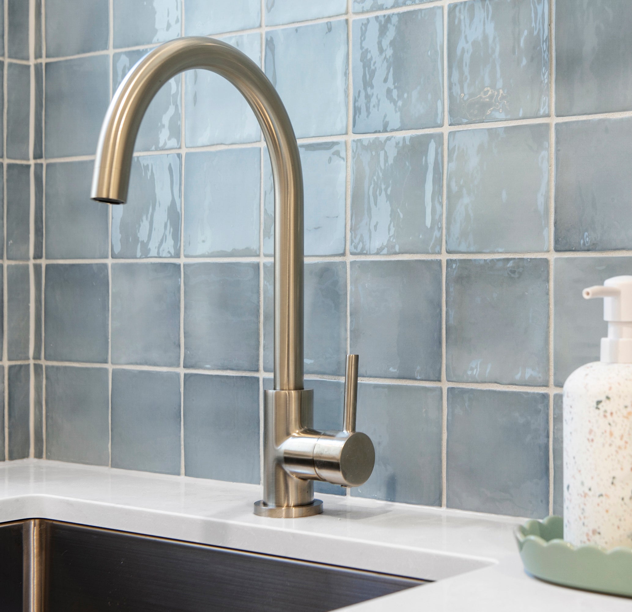 a brushed nickel kitchen laundry mixer on a white bench with a blue tile background