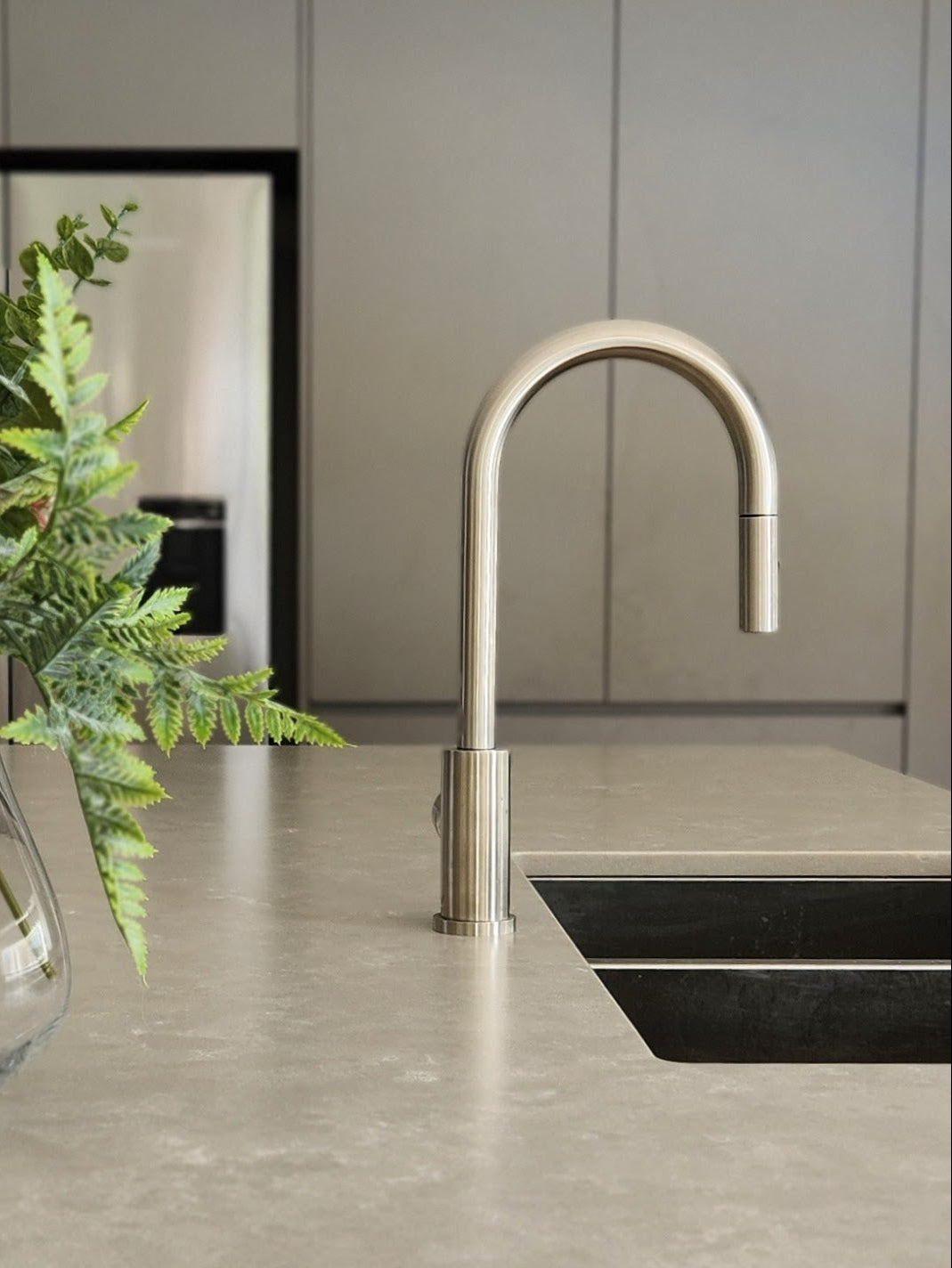 a brushed nickel kitchen laundry pull out mixer tap on a modern kitchen countertop with a vase of flowers