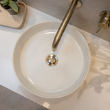White round sink with a brushed nickel pop up waste with no overflow t on a light-colored countertop.