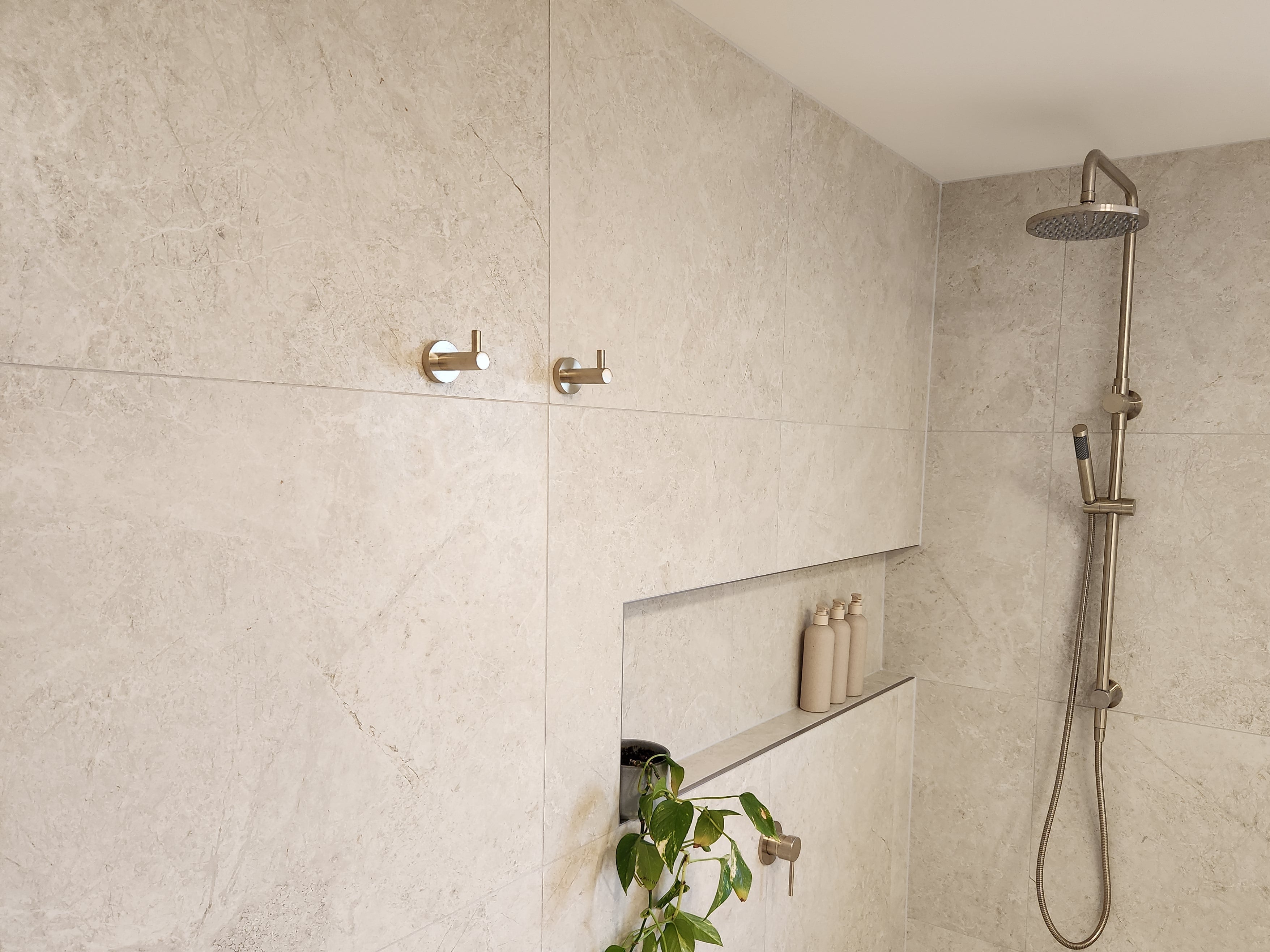 Shower area with tiled walls, a brushed nickel twin shower and diverter, brushed nickel robe hooks with a niche.