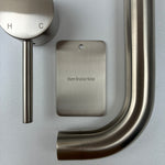 Brushed nickel bathroom fixtures including a sample disc, wall mixer and wall spout  on a grey background.