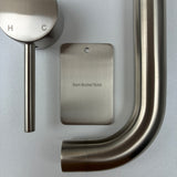 Brushed nickel bathroom fixtures including a sample disc, wall mixer and wall spout  on a grey background.