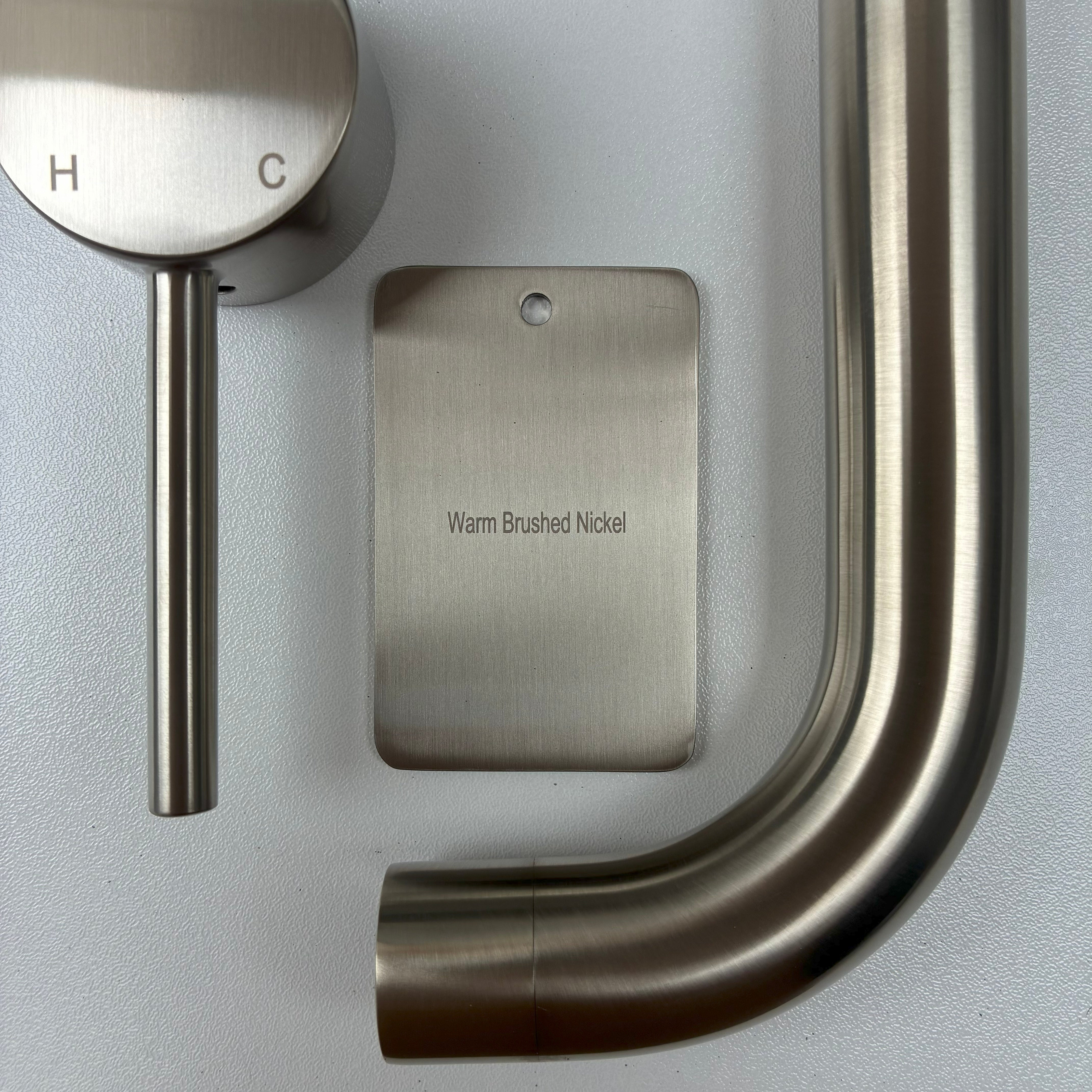 Brushed nickel bathroom fixtures including a sample disc, wall mixer and wall spout  on a grey background.