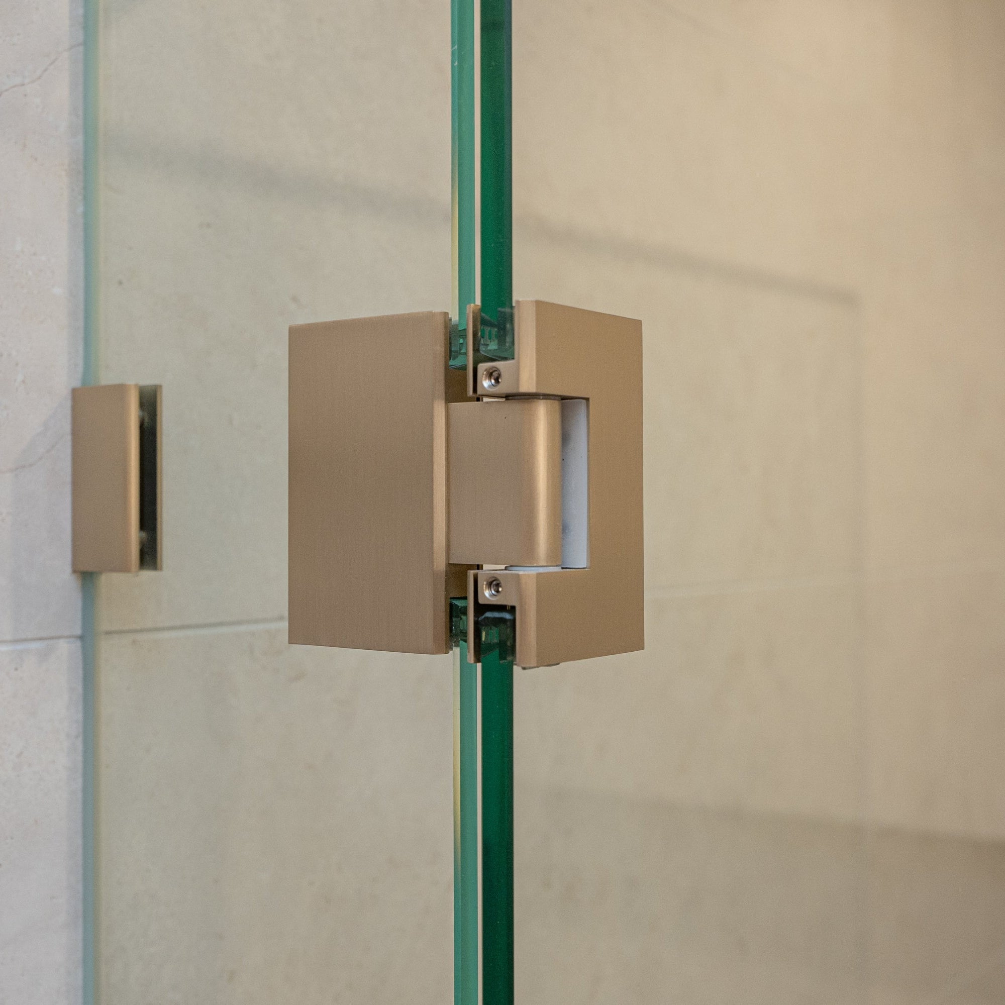 Brushed nickel shower door hinge on a glass shower door with tiled wall background.