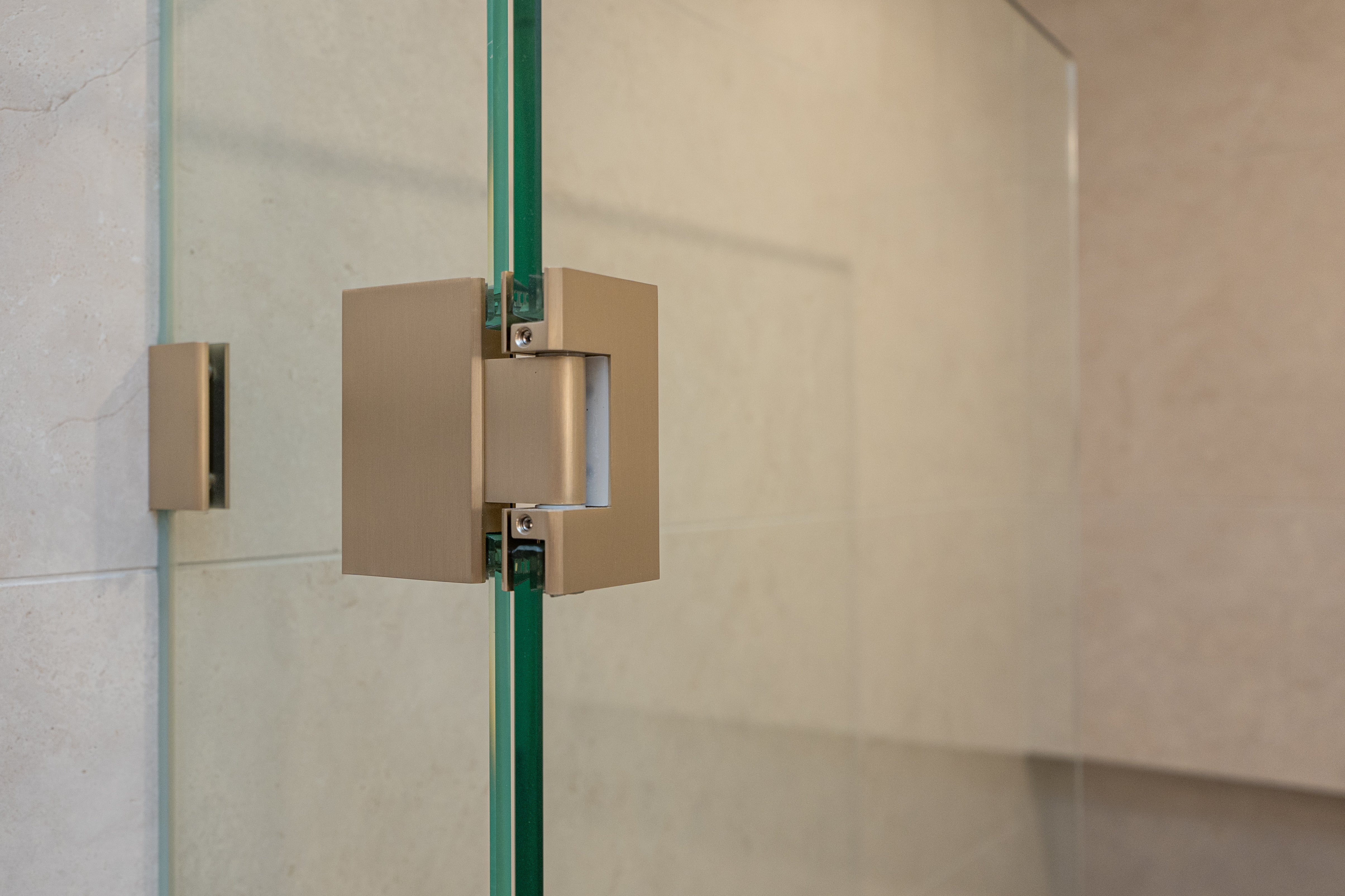 Brushed nickel shower door hinge on a glass shower door with tiled wall background.