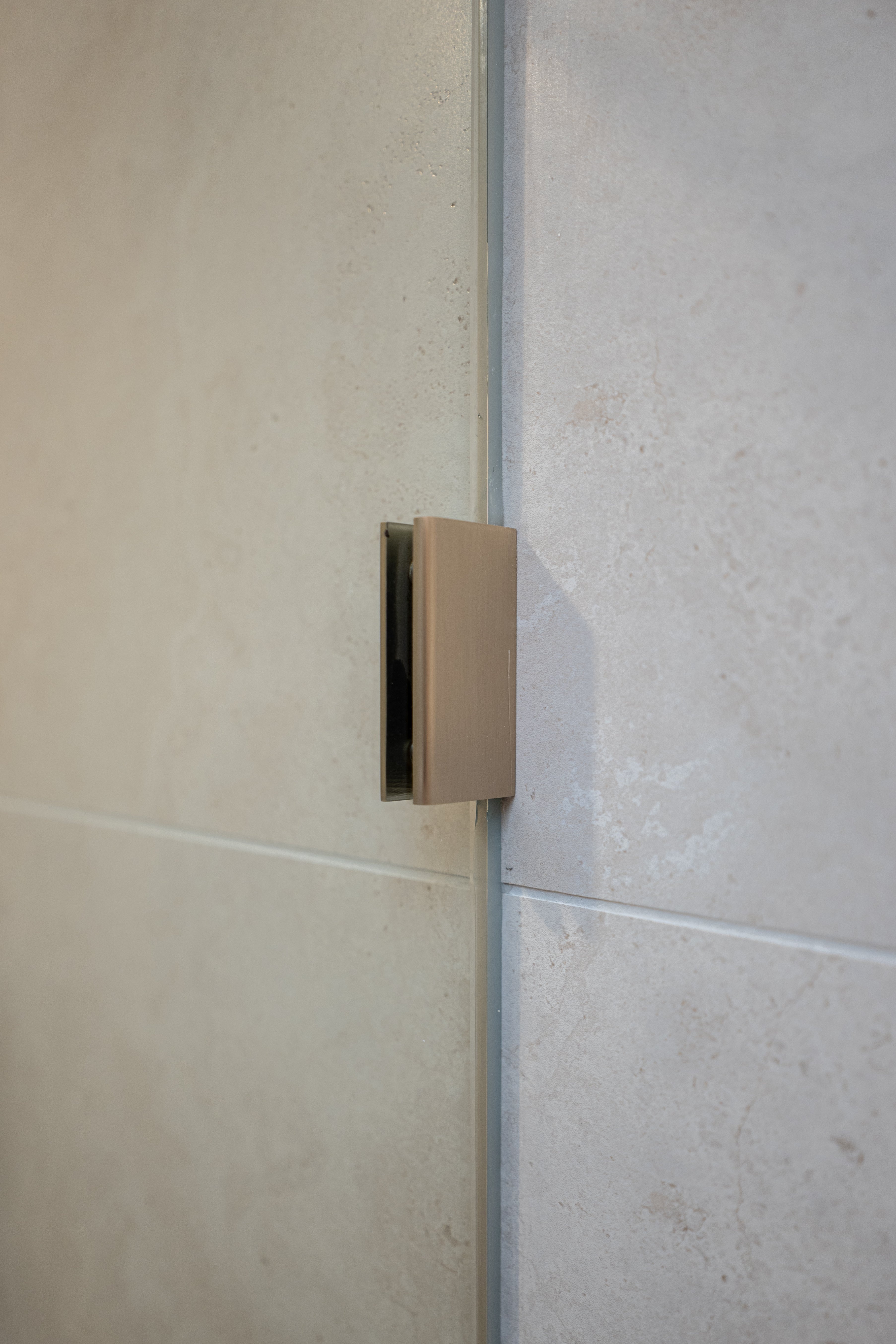 Brushed nickel shower glass clamp on a tiled wall.