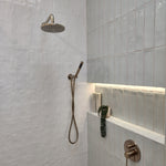 a brushed nickel shower handpiece on a bracket wall mounted on a tiled bathroom wall