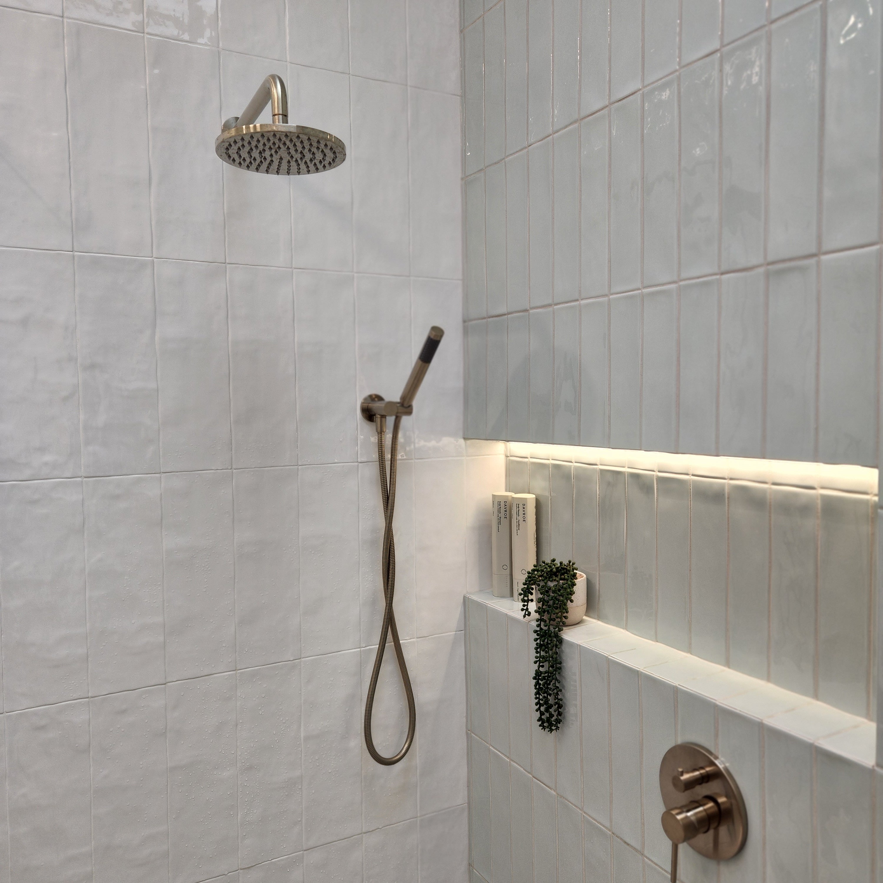 a brushed nickel shower handpiece on a bracket wall mounted on a tiled bathroom wall