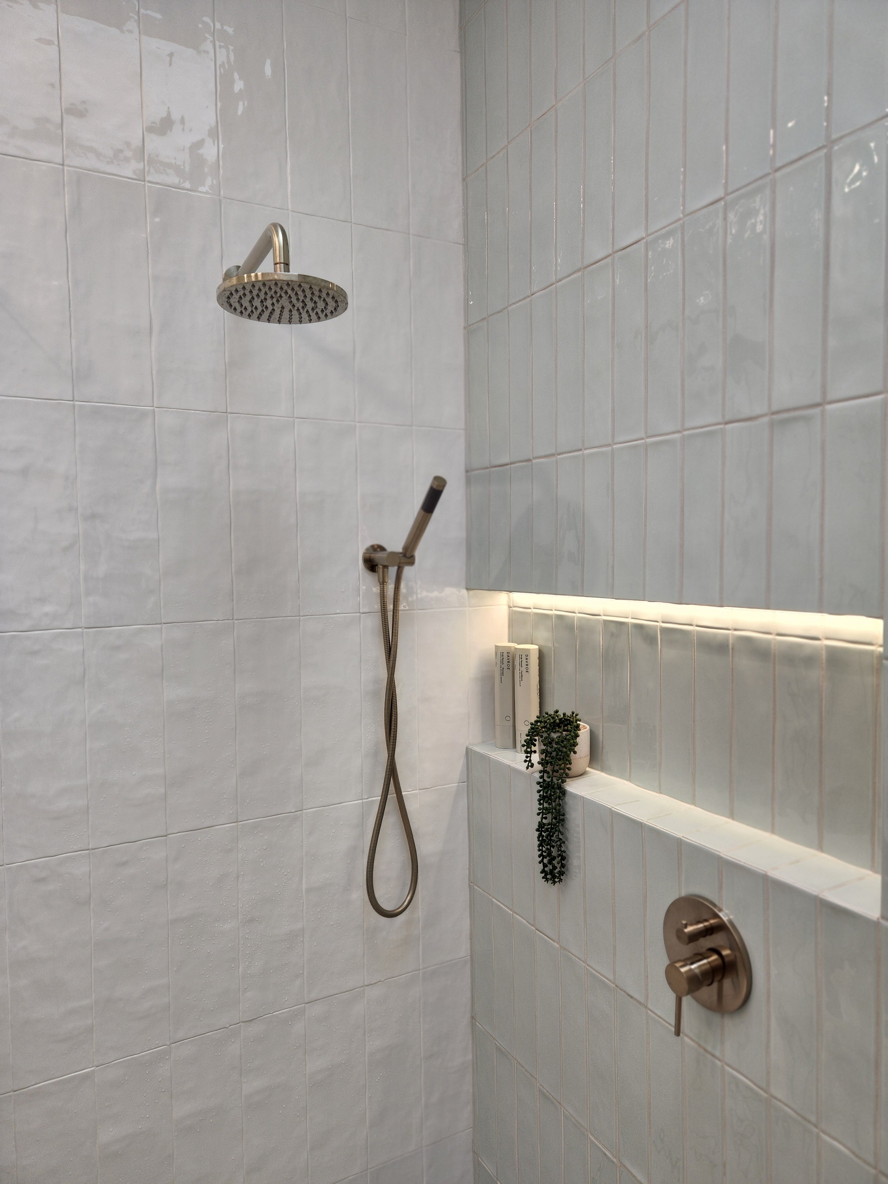 a brushed nickel shower handpiece on a bracket wall mounted on a tiled bathroom wall