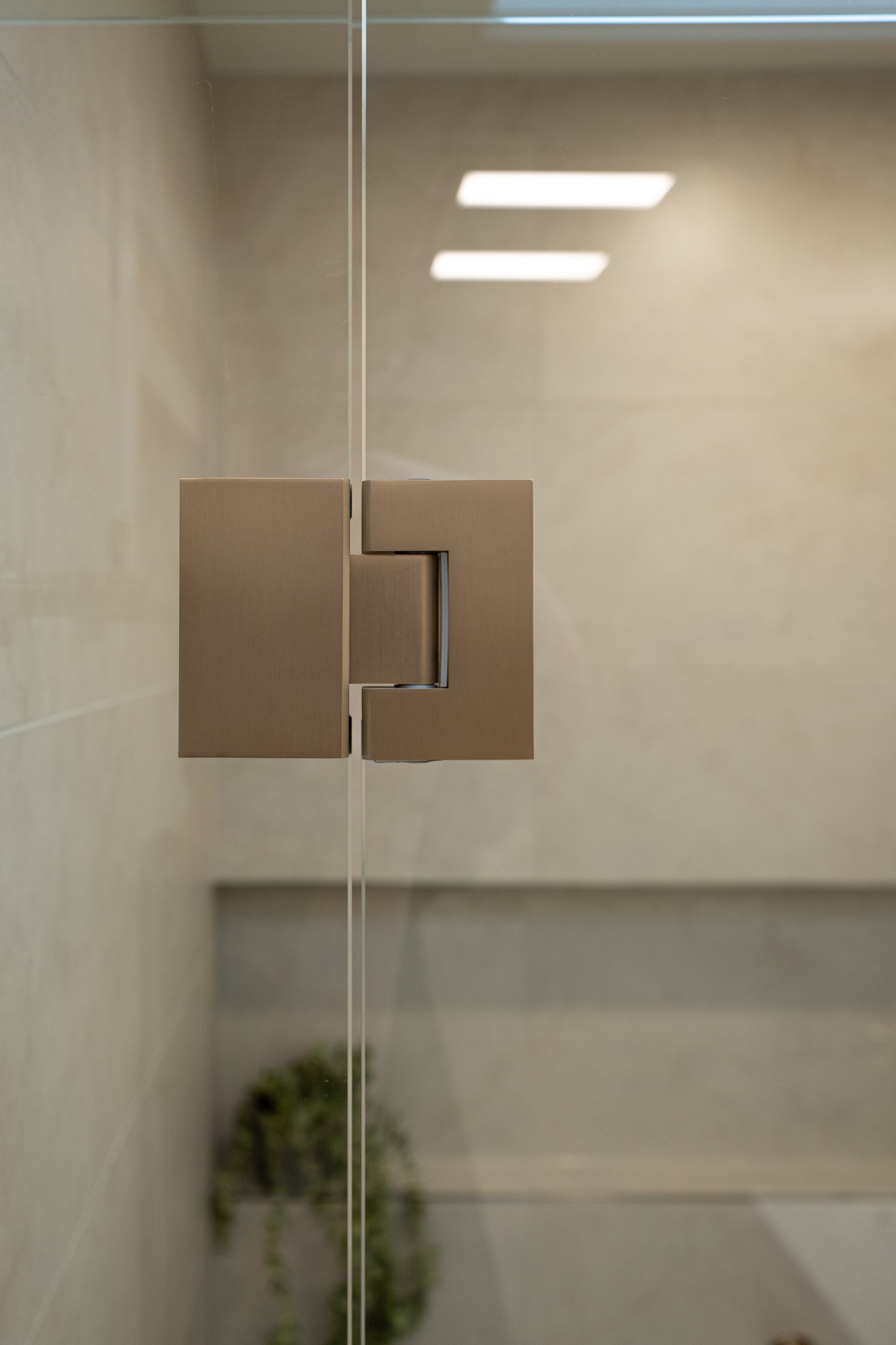 Brushed nickel shower glass hinge with glass shower  and tiled wall.