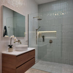 a brushed nickel shower head on wall in a modern bathroom with glass shower enclosure, wooden cabinet, and sink.