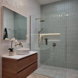 a brushed nickel shower head on wall in a modern bathroom with glass shower enclosure, wooden cabinet, and sink.