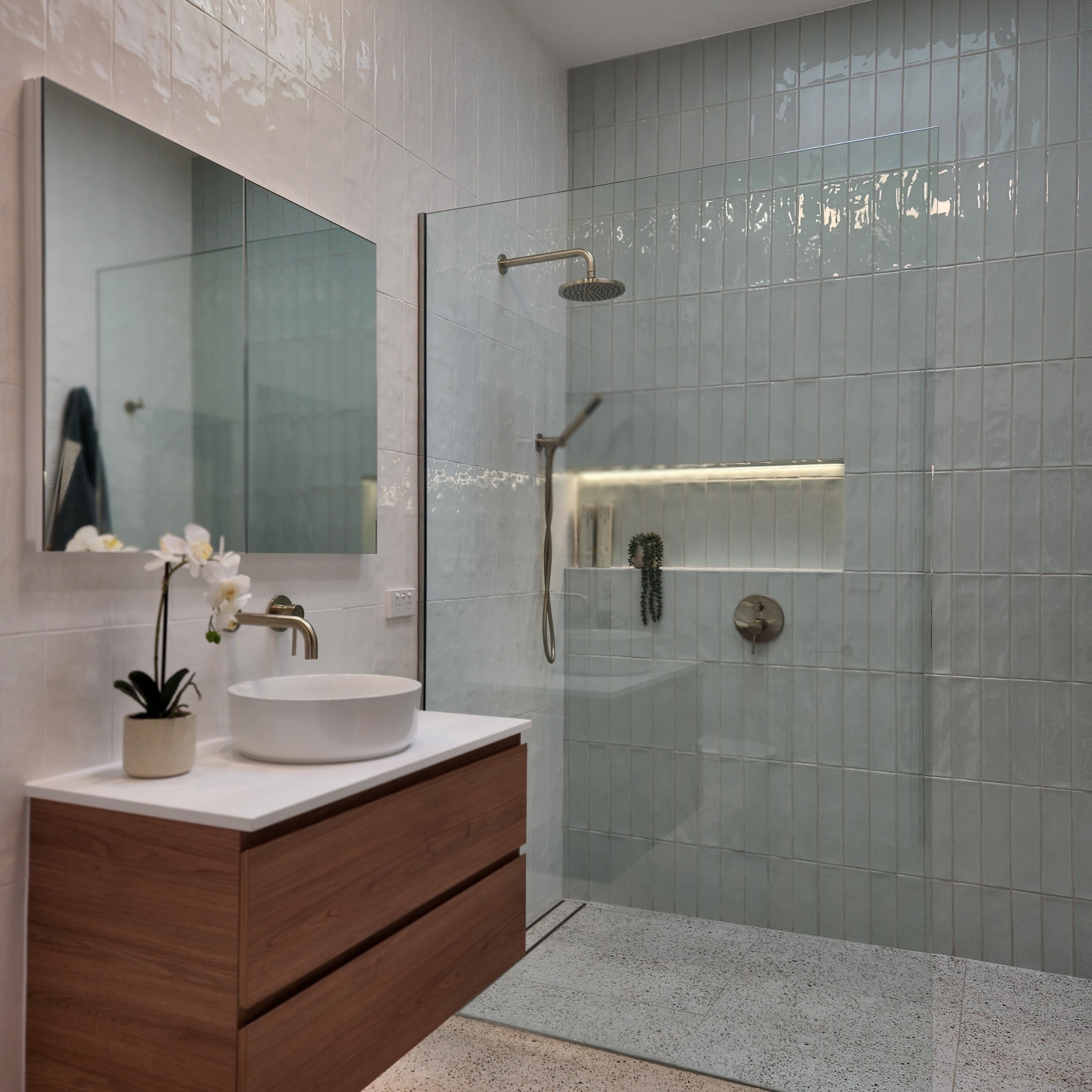 a brushed nickel shower head on wall in a modern bathroom with glass shower enclosure, wooden cabinet, and sink.