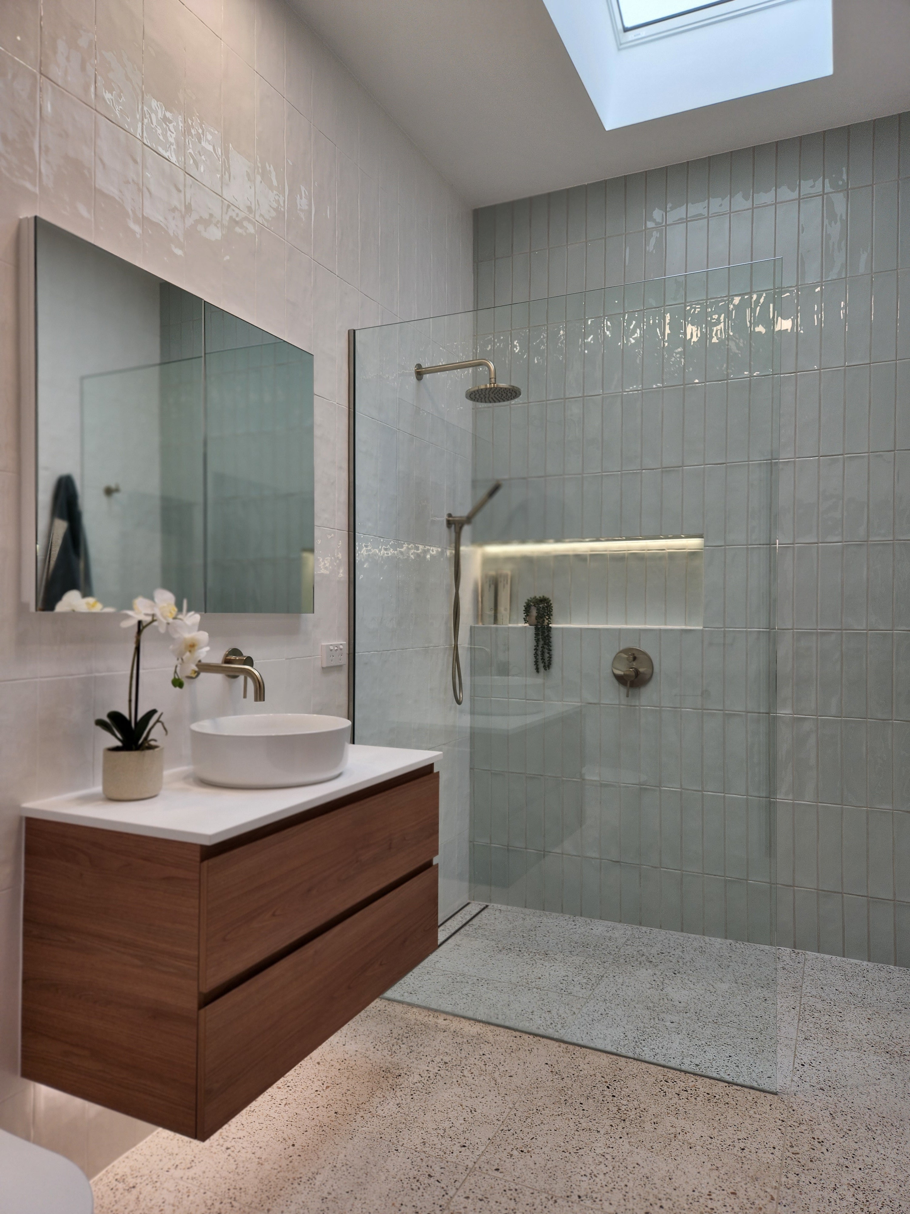 a brushed nickel shower head on wall in a modern bathroom with glass shower enclosure, wooden cabinet, and sink.