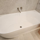 Brushed nickel swivel bath spout with white freestanding bathtub in a bathroom with tiled walls and wooden cabinet.