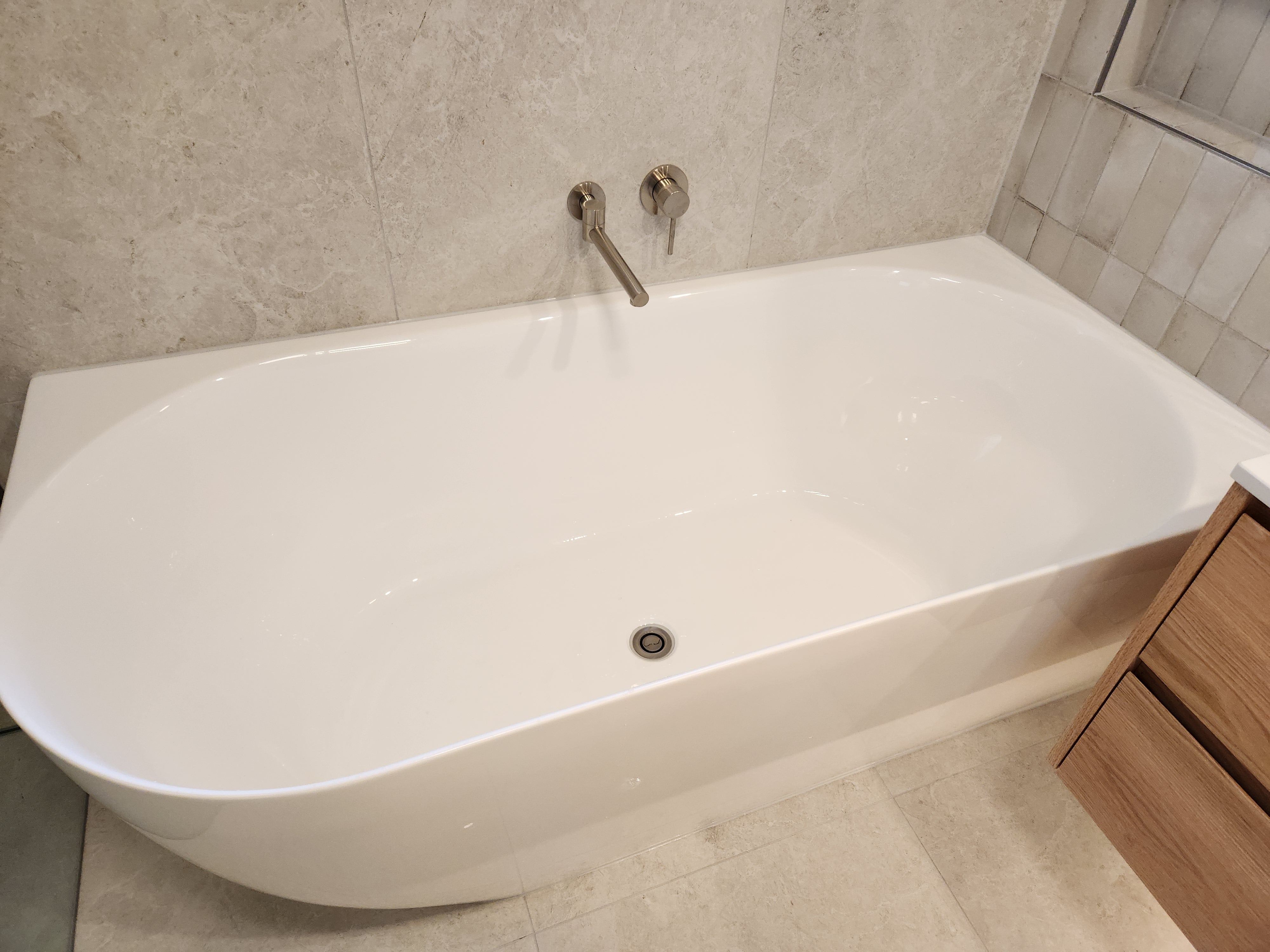 Brushed nickel swivel bath spout with white freestanding bathtub in a bathroom with tiled walls and wooden cabinet.