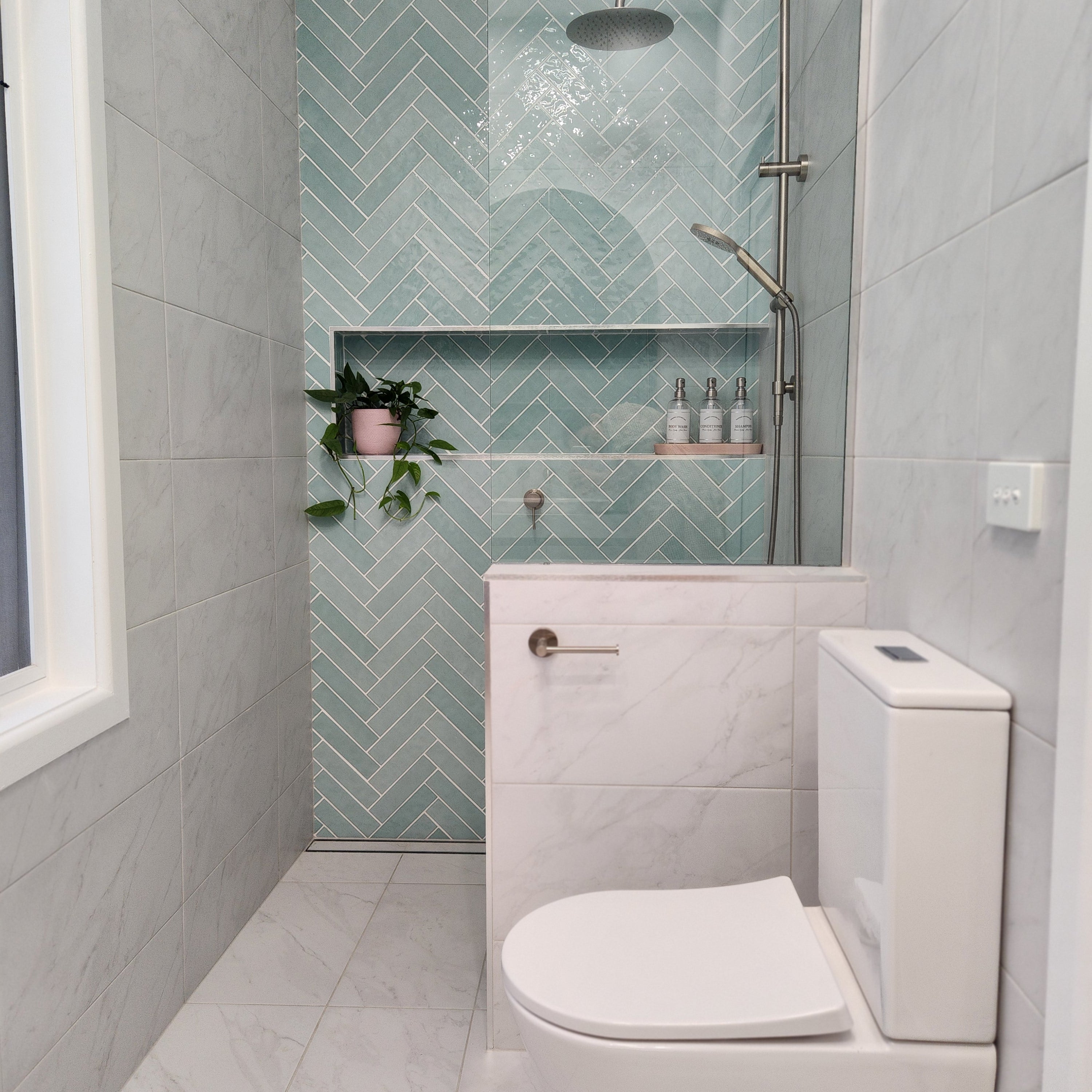 a brushed nickel toilet roll holder in a bathroom with white toilet, green tiled wall, and small plant.