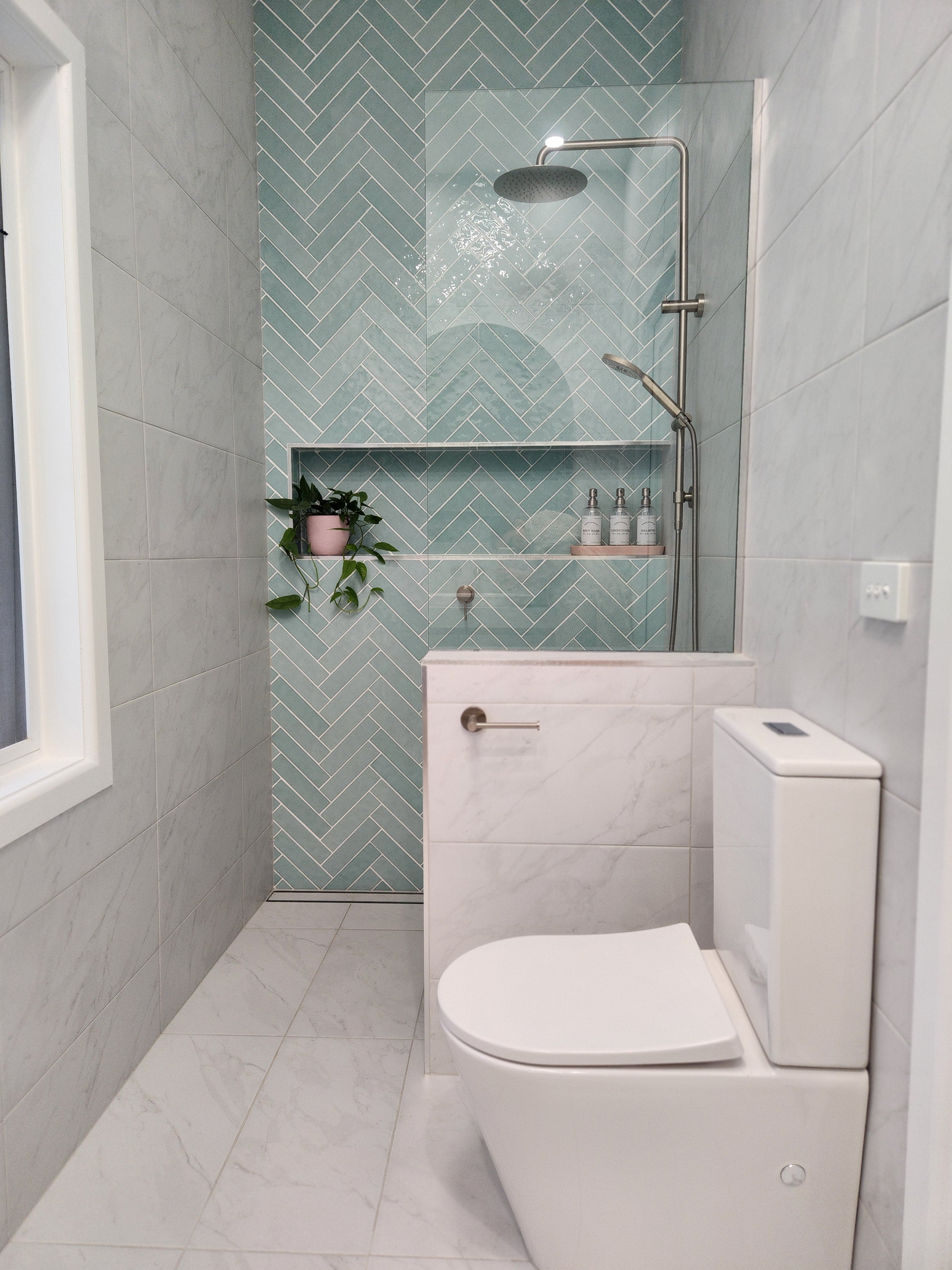 a brushed nickel toilet roll holder in a bathroom with white toilet, green tiled wall, and small plant.