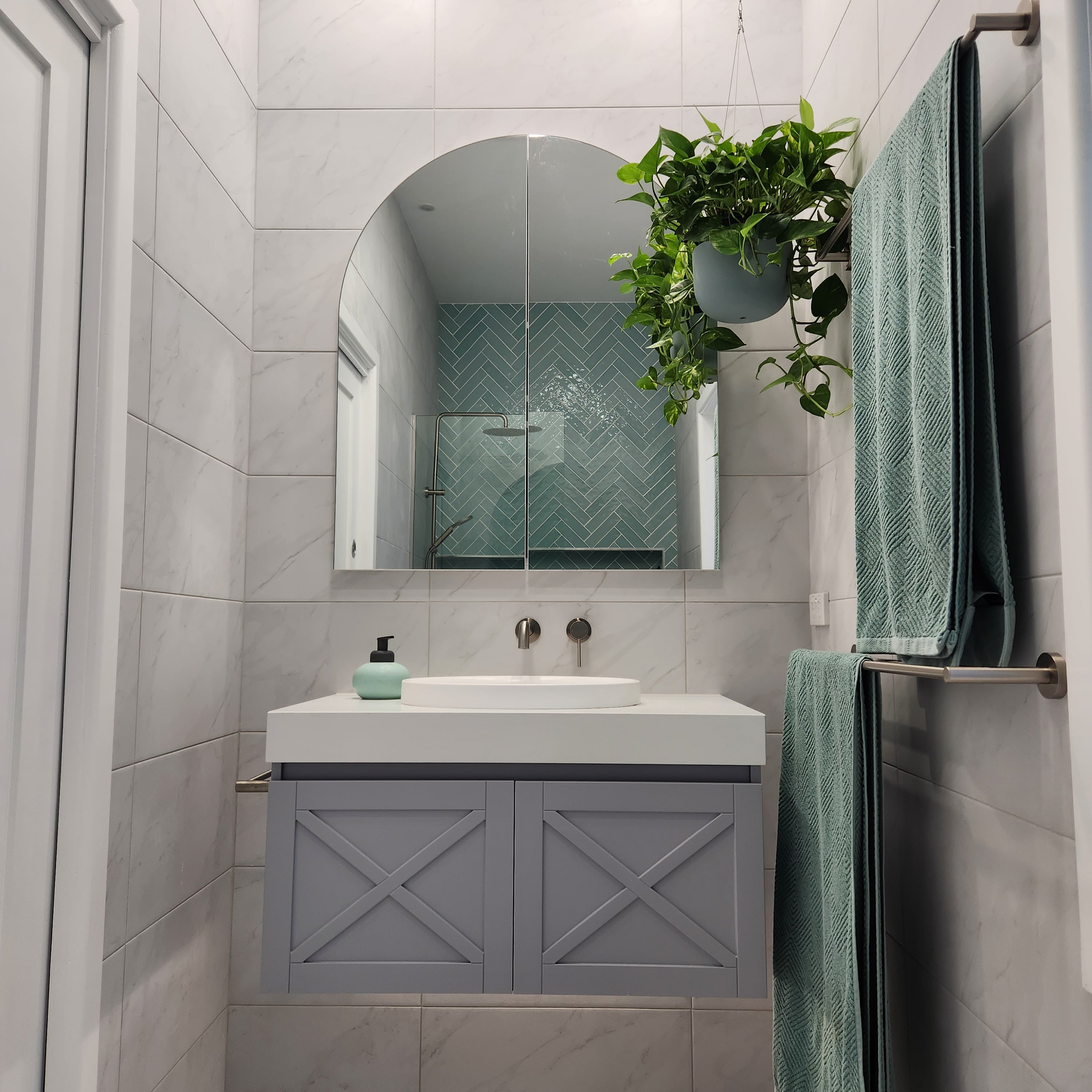 a set of brushed nickel towel rails in a bathroom interior with a sink, mirror, and plant