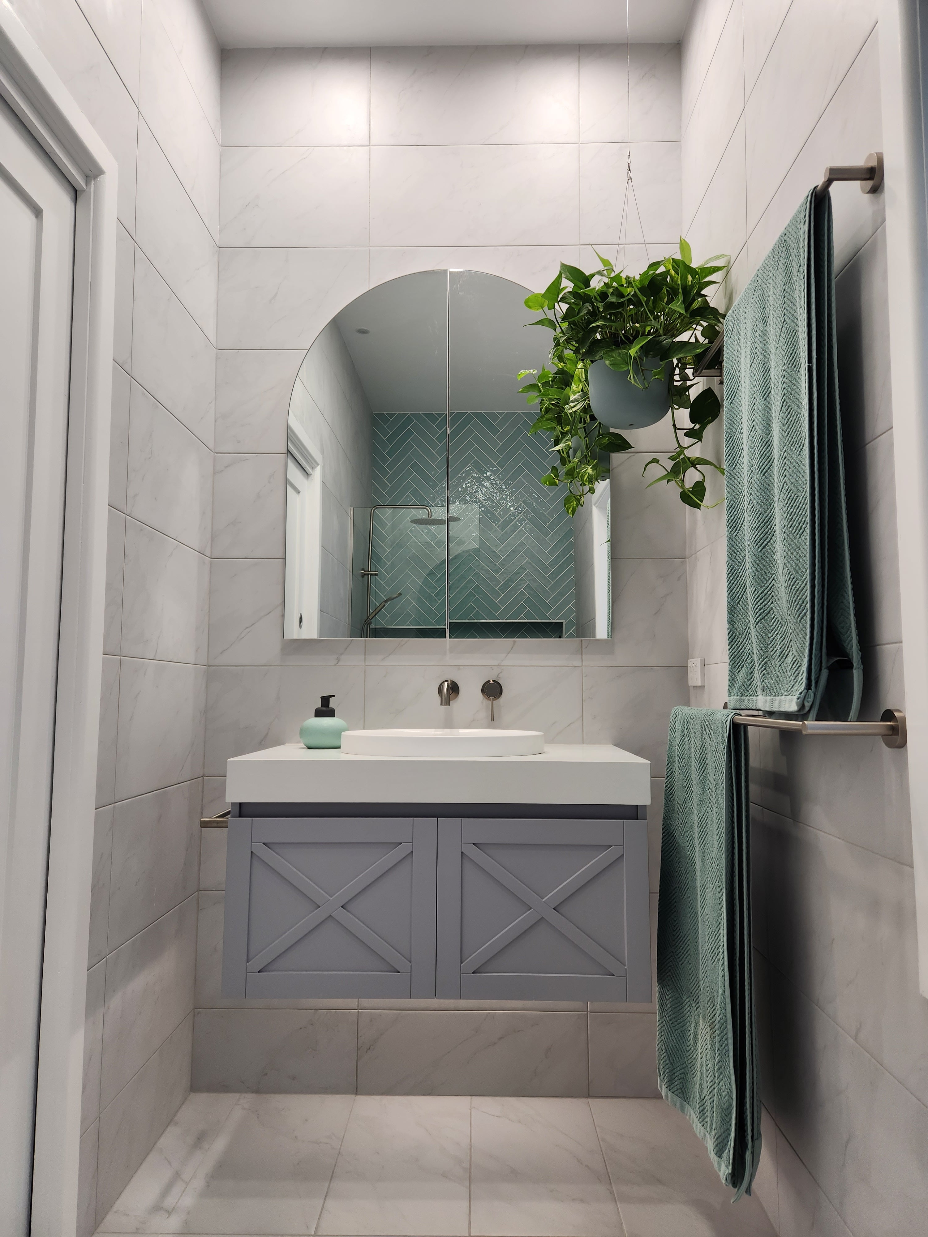 a set of brushed nickel towel rails in a bathroom interior with a sink, mirror, and plant