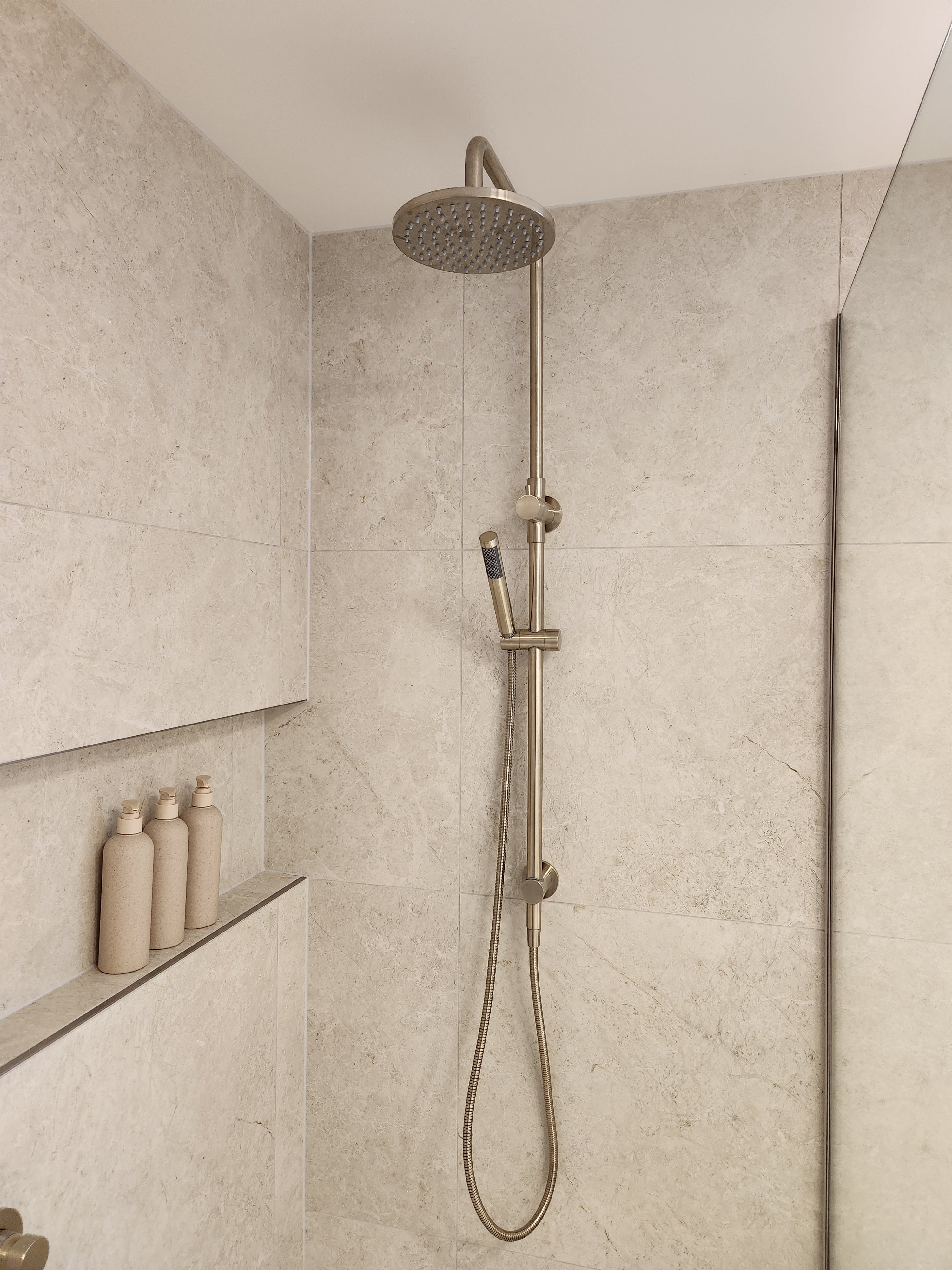 Brushed nickel twin shower with diverter on a tiled bathroom wall