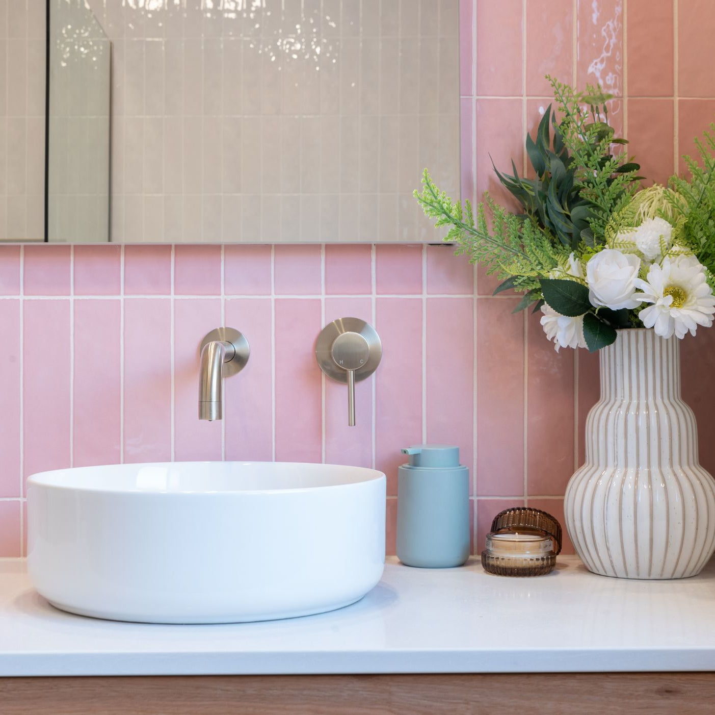 a brushed nickel wall mixer and spout on a pink tiled background