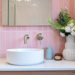 a brushed nickel wall mixer and spout on a pink tiled background